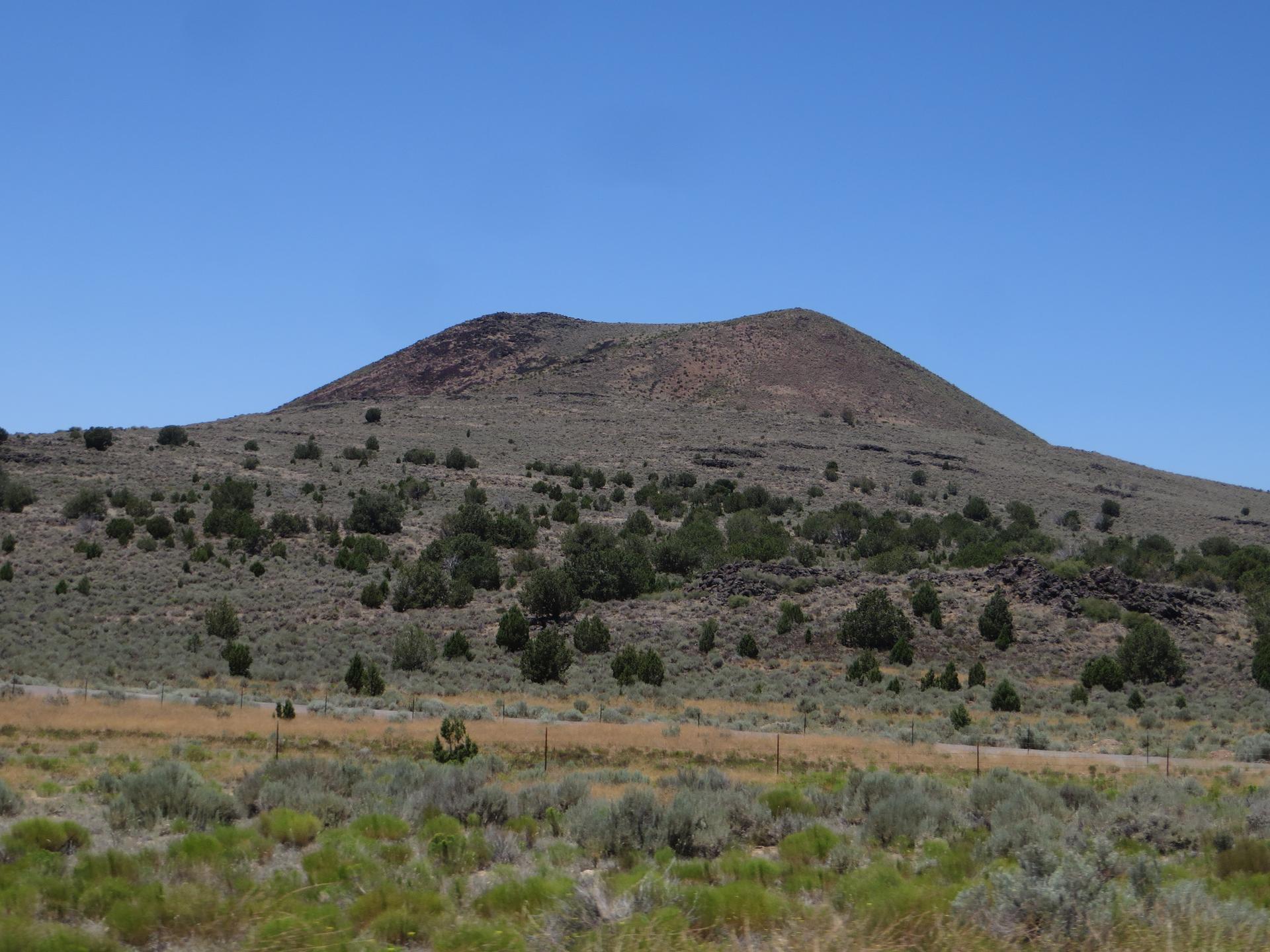 A large, barren hill covered in sparse green shrubs under a clear blue sky.