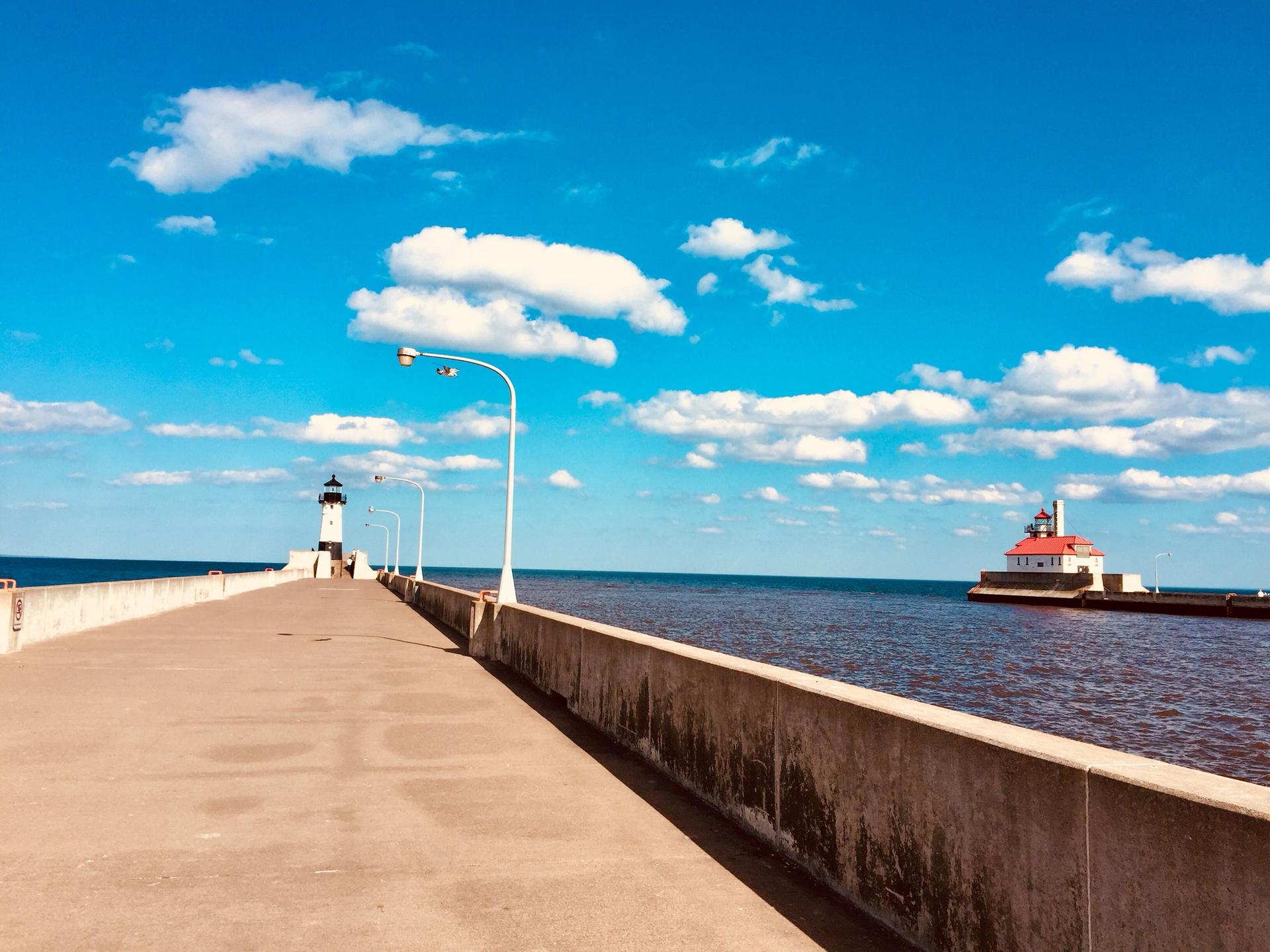 Two lighthouses and a long pier under a bright blue sky.