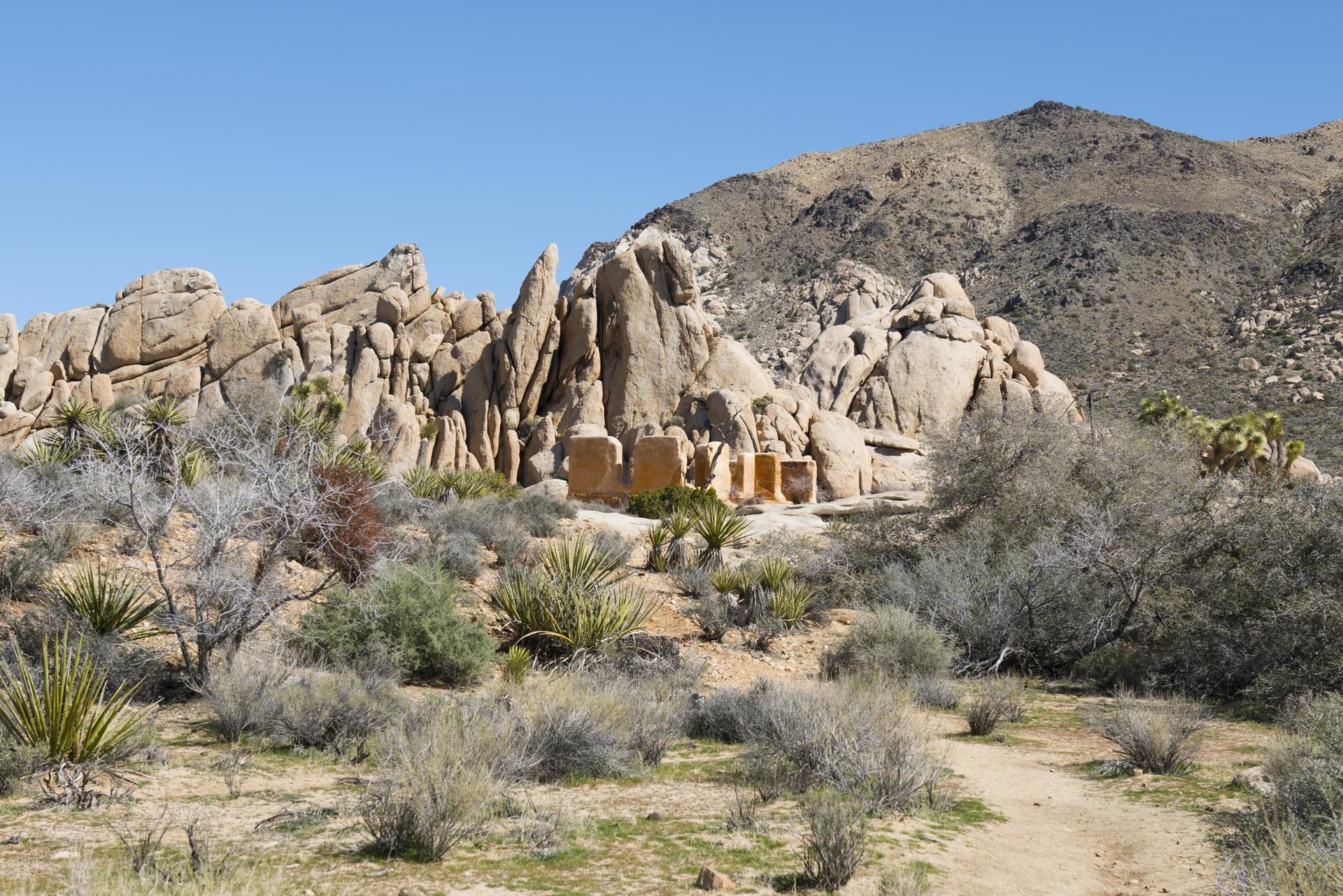 Massive rock formations rise from a desert landscape under a clear blue sky.