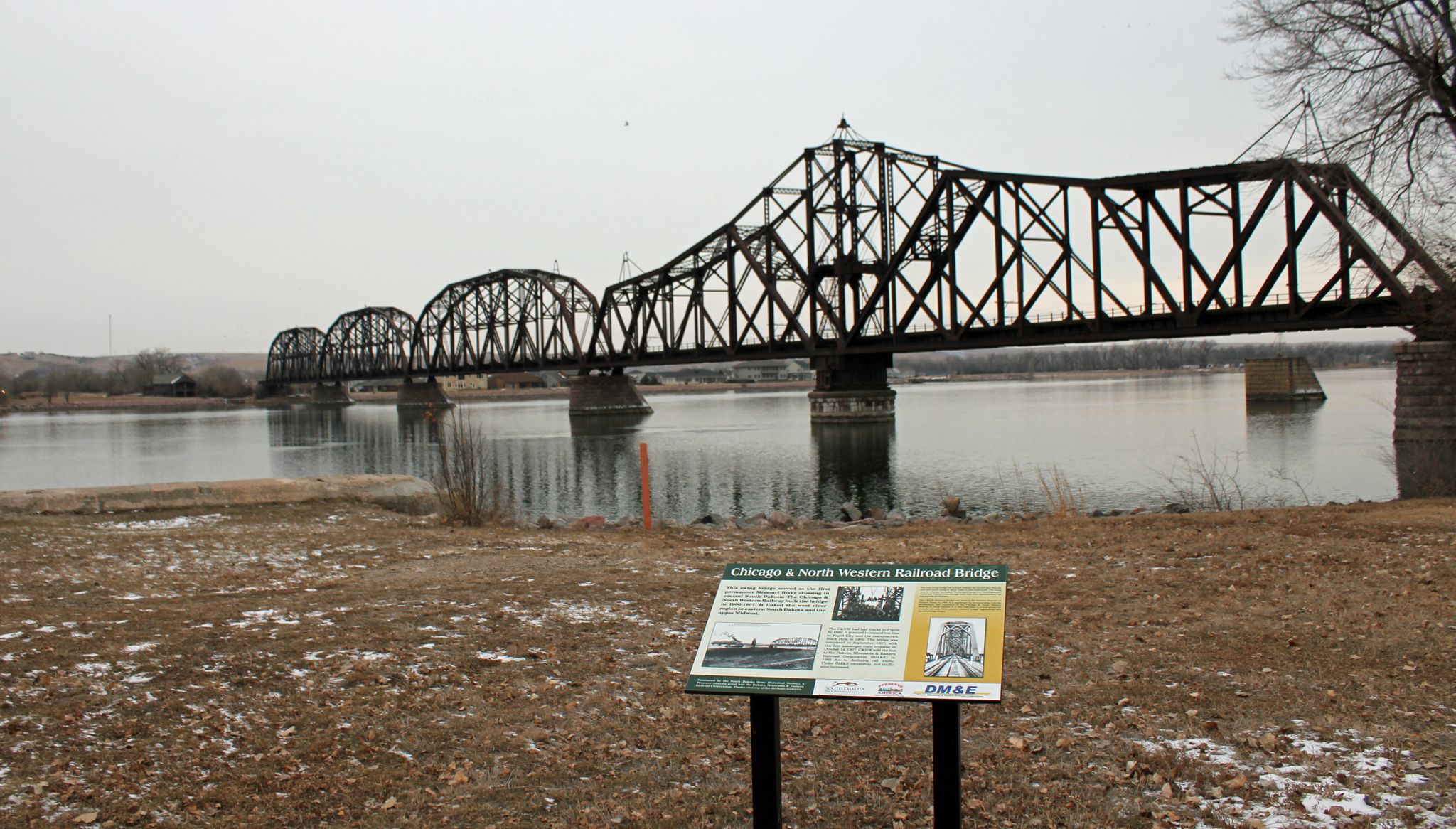 Large metal truss bridge over a river, with an informational sign in foreground. - Lewis and Clark Bicentennial Trail