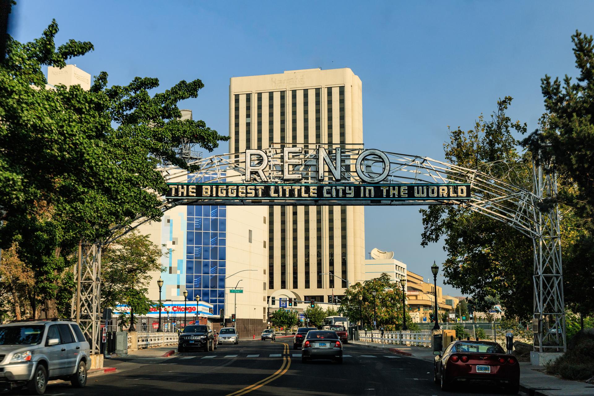 City street with a large archway sign, cars, and tall buildings under bright sky.