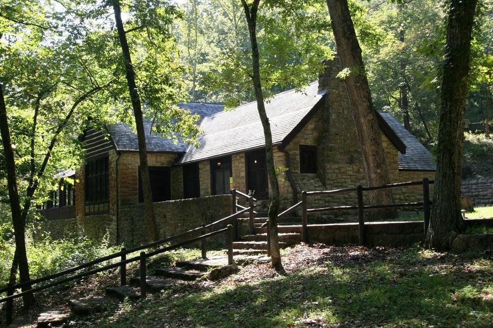 Rustic stone cabin nestled in a sun-dappled forest with a wooden fence.