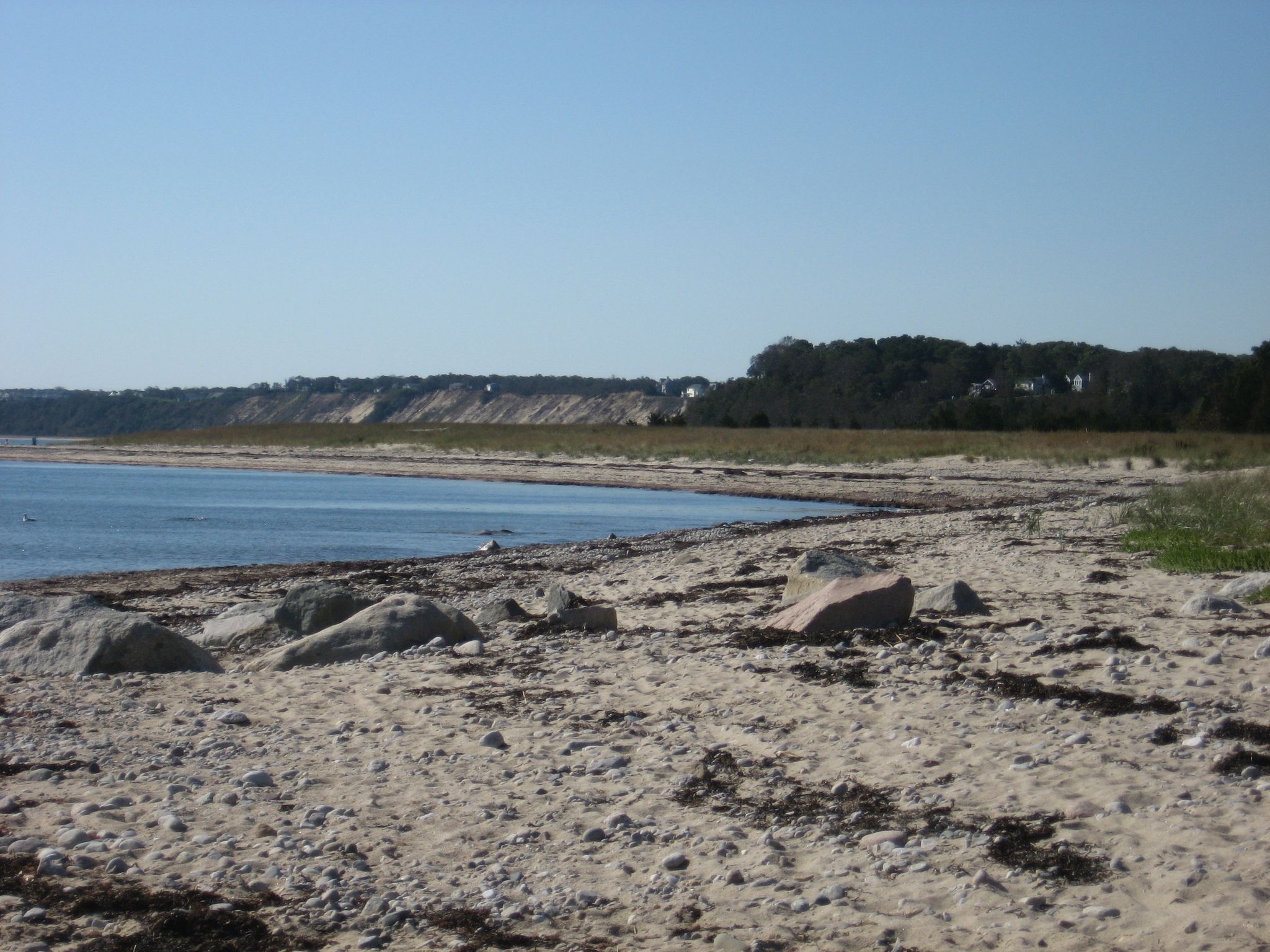 Sandy beach with rocks and distant dunes under a clear blue sky. - Plymouth Wishbone Trail
