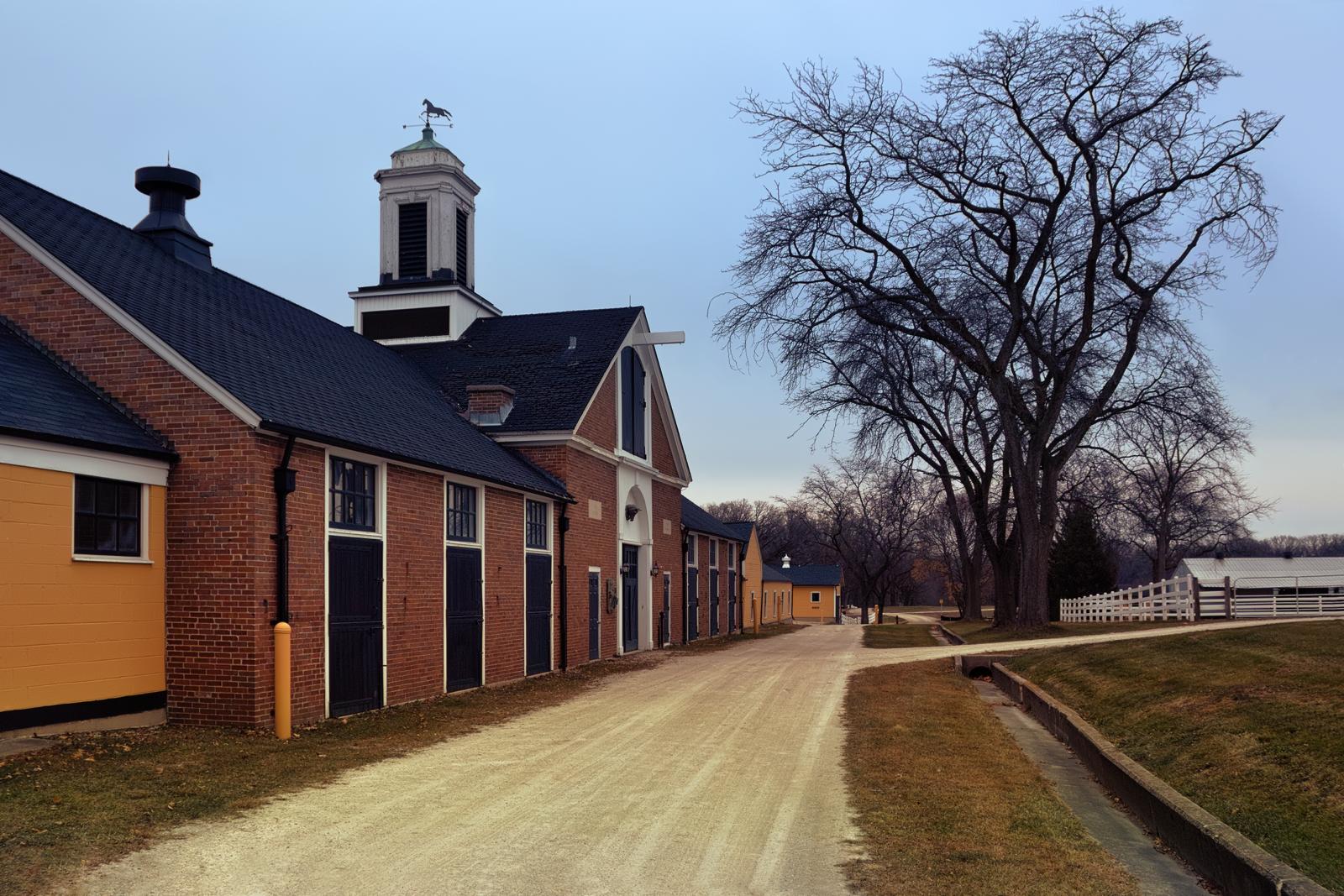 Large brick and yellow buildings with a cupola along a dirt road under an overcast sky.