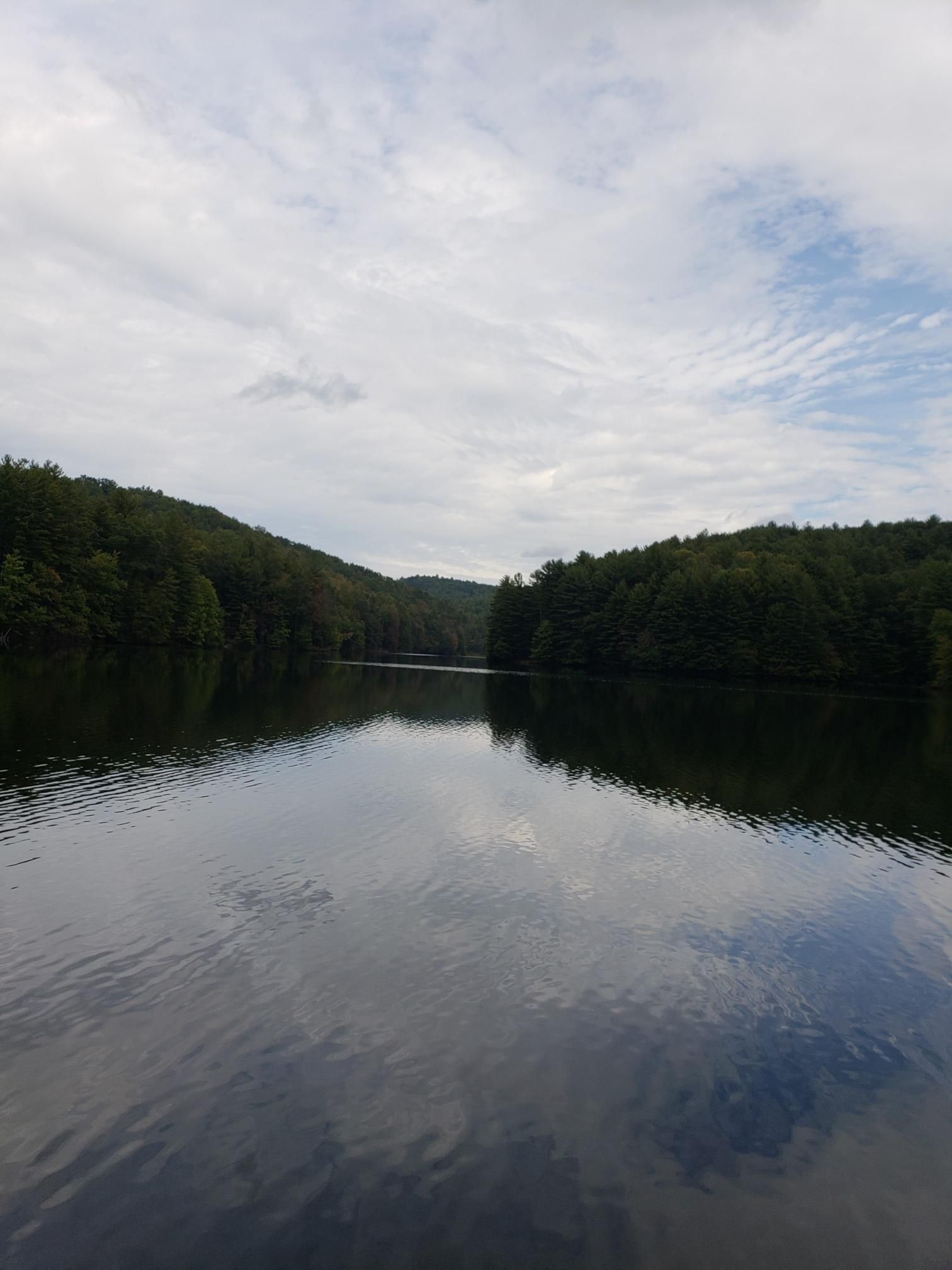 Calm lake reflecting forested hills under a bright, cloudy sky. - Reasonover Creek Loop