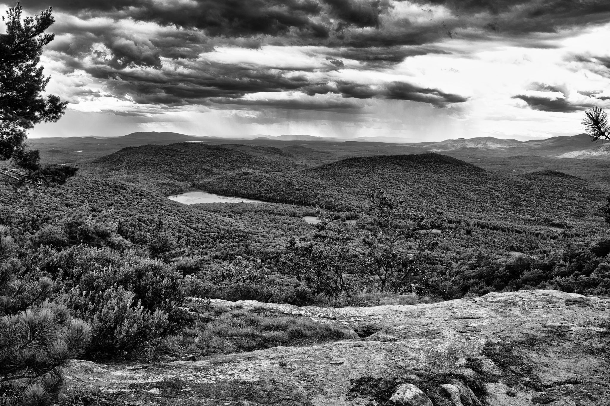Black and white mountain vista with dense forests, a lake, and dramatic clouds. - Evans Notch and Blueberry Mountain Loop Trail