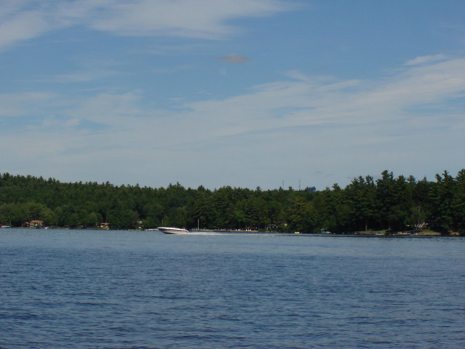 A boat speeds across a wide blue lake under a clear sky.