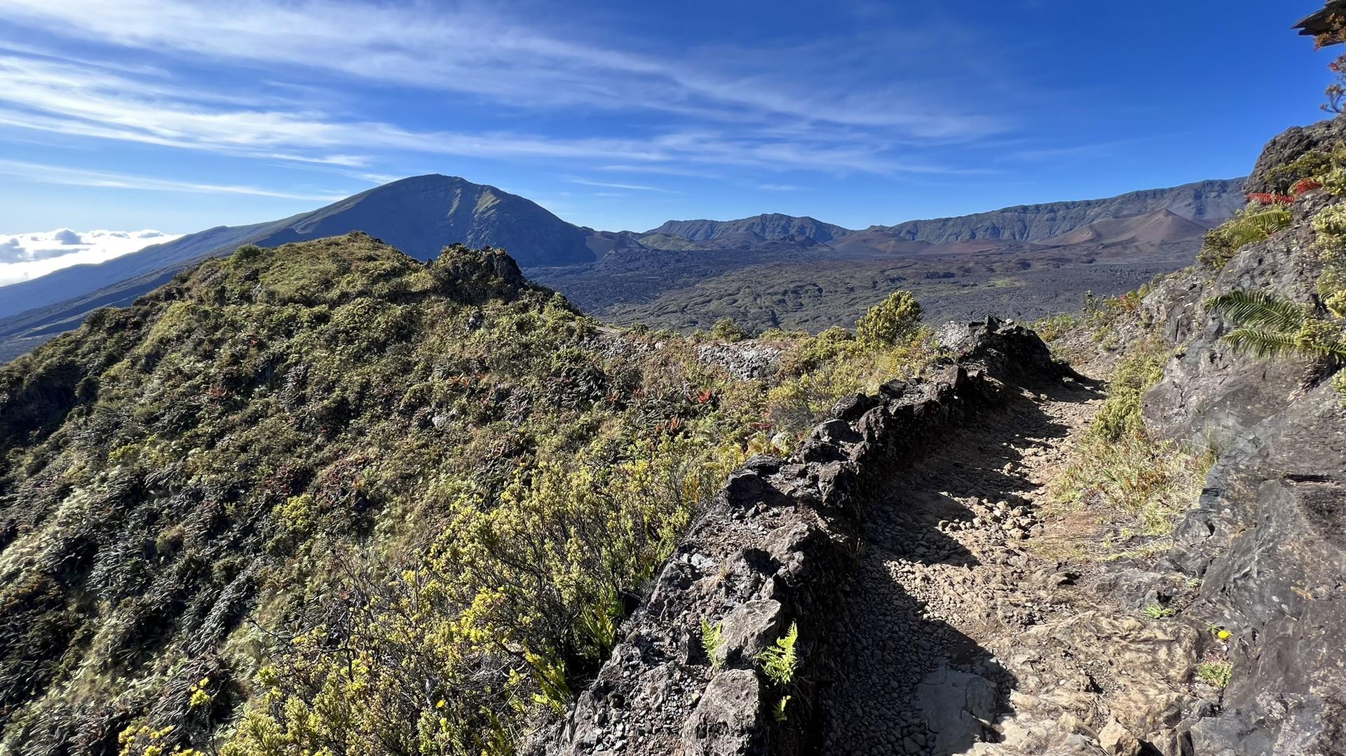 A rocky mountain trail with distant peaks under a clear blue sky.