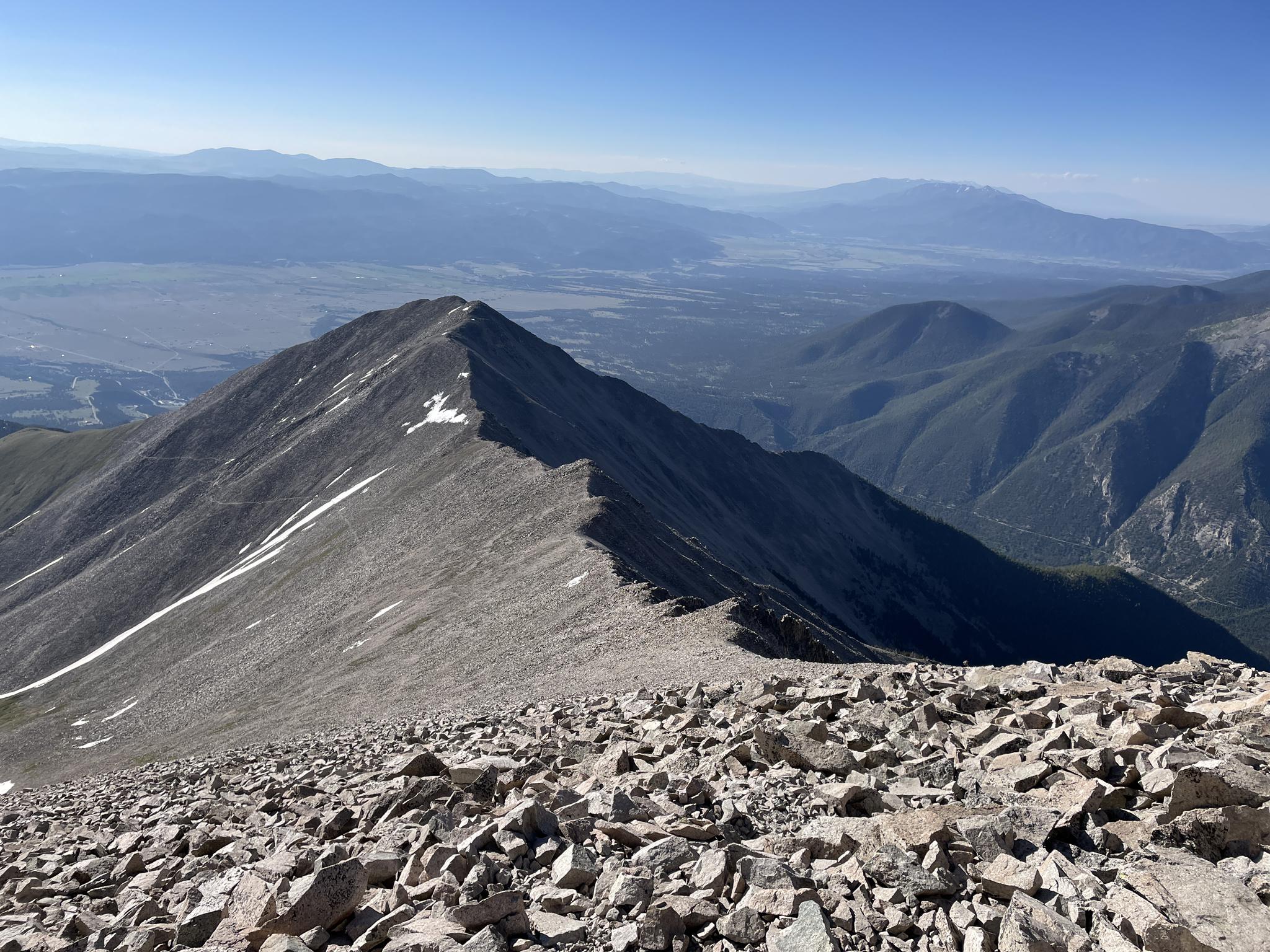 Steep, rocky mountain ridge under a clear sky with distant valleys.