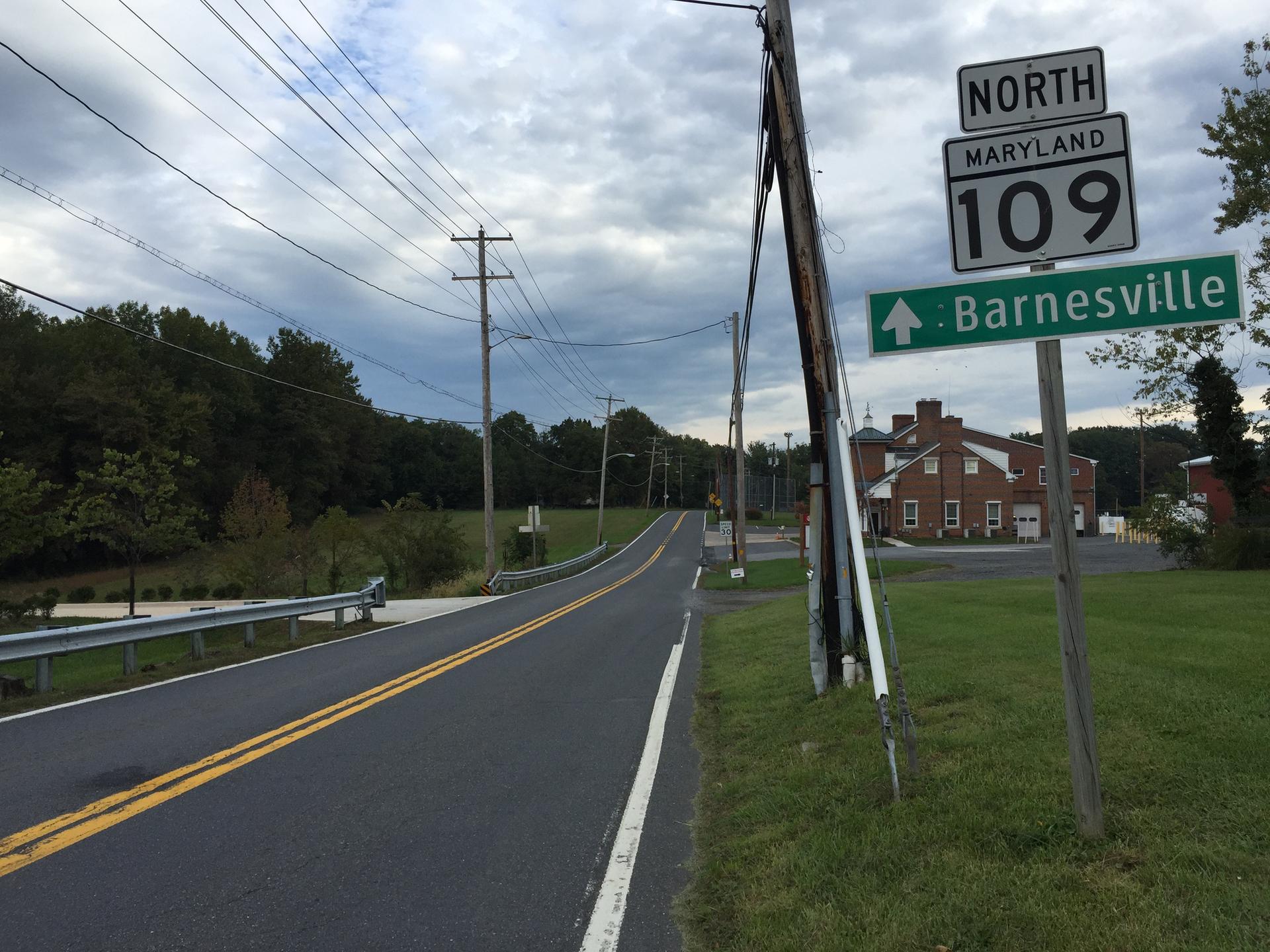 Rural road with power lines and a street sign under an overcast sky.