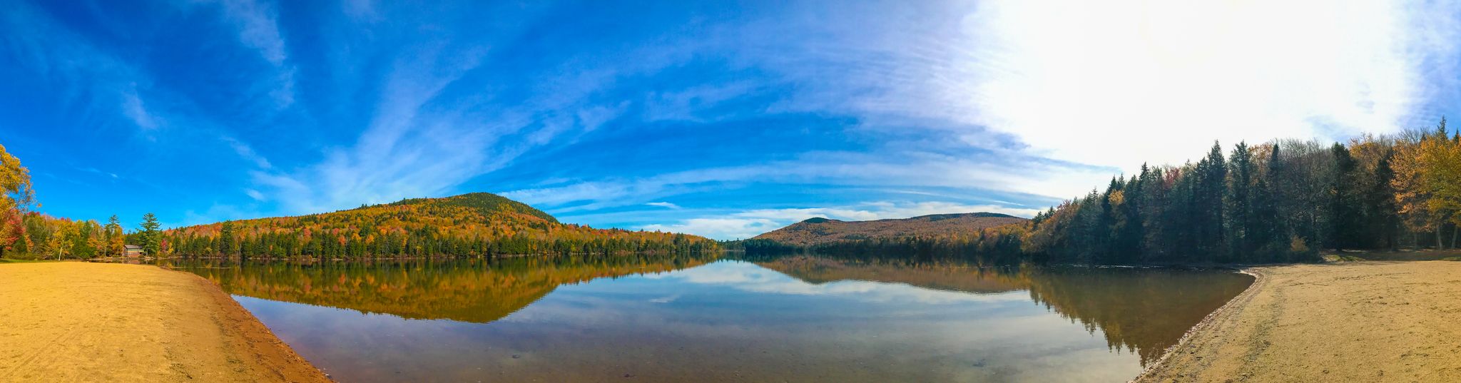 Panoramic view of a calm lake reflecting colorful autumn trees under a bright blue sky. - Christine Lake to South Pond