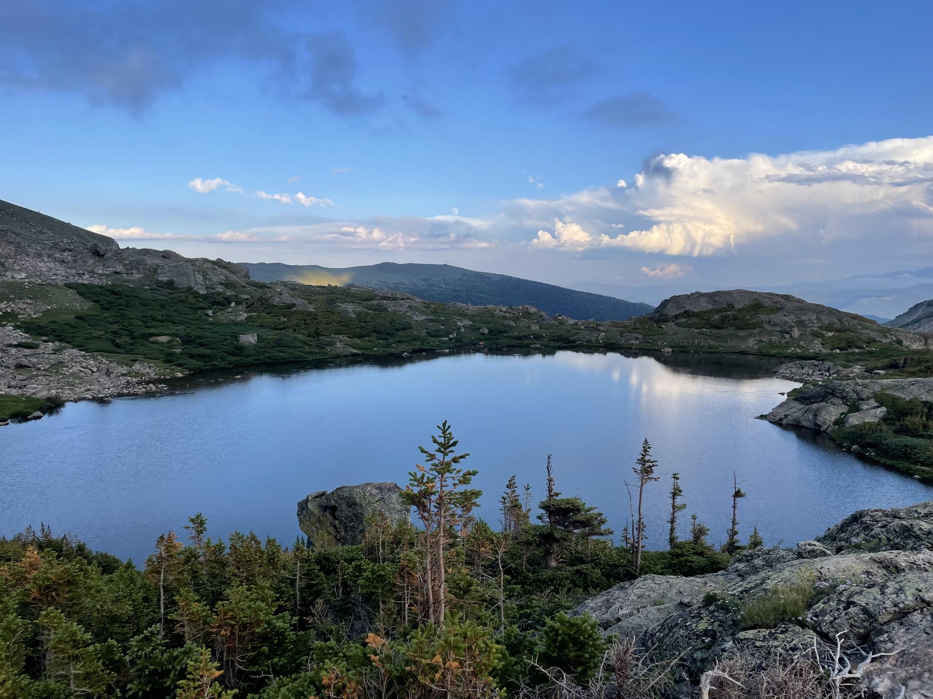A serene mountain lake surrounded by rocky, forested hills under a bright sky.