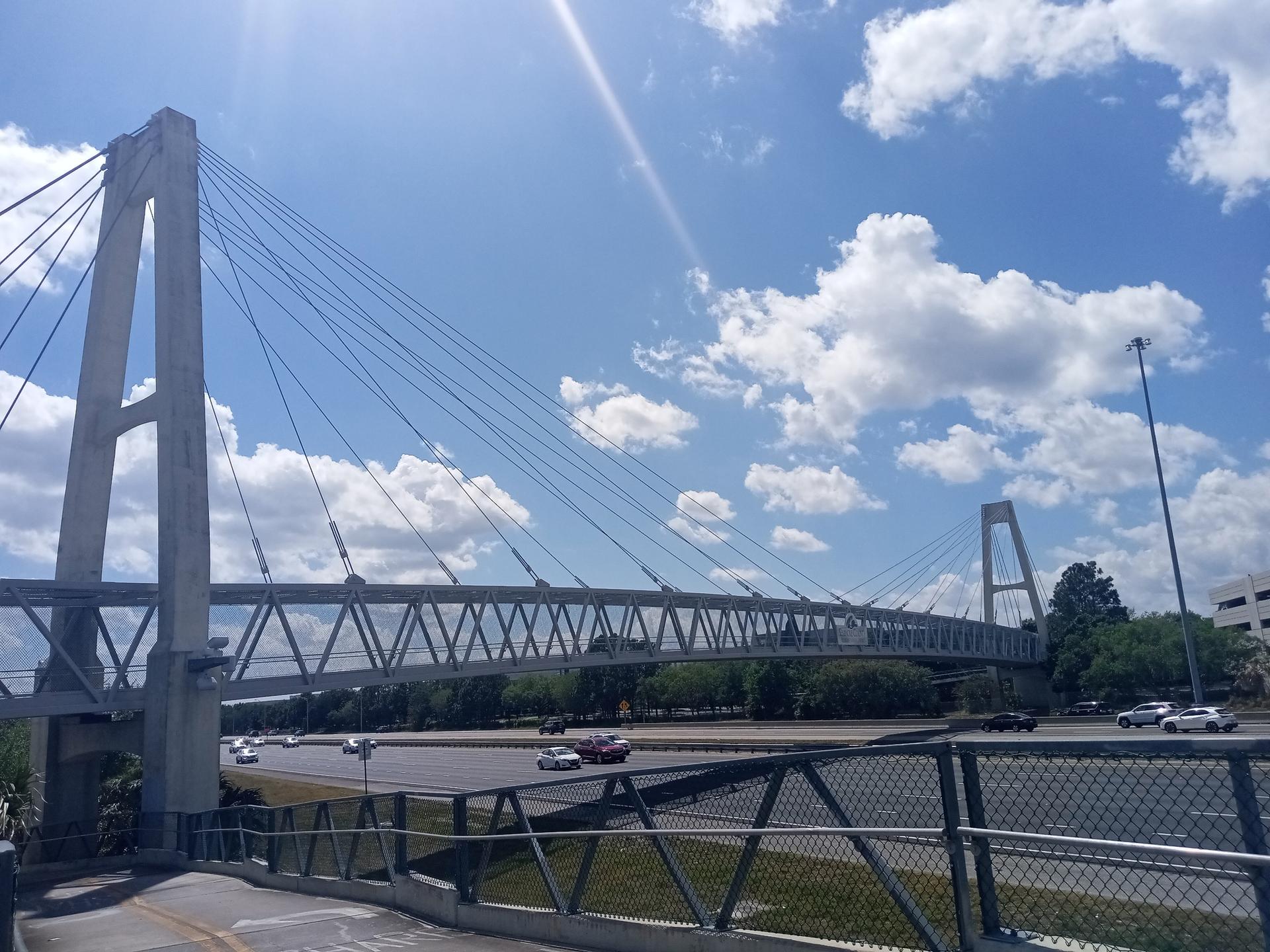 A large suspension bridge spans over a busy highway on a sunny day.