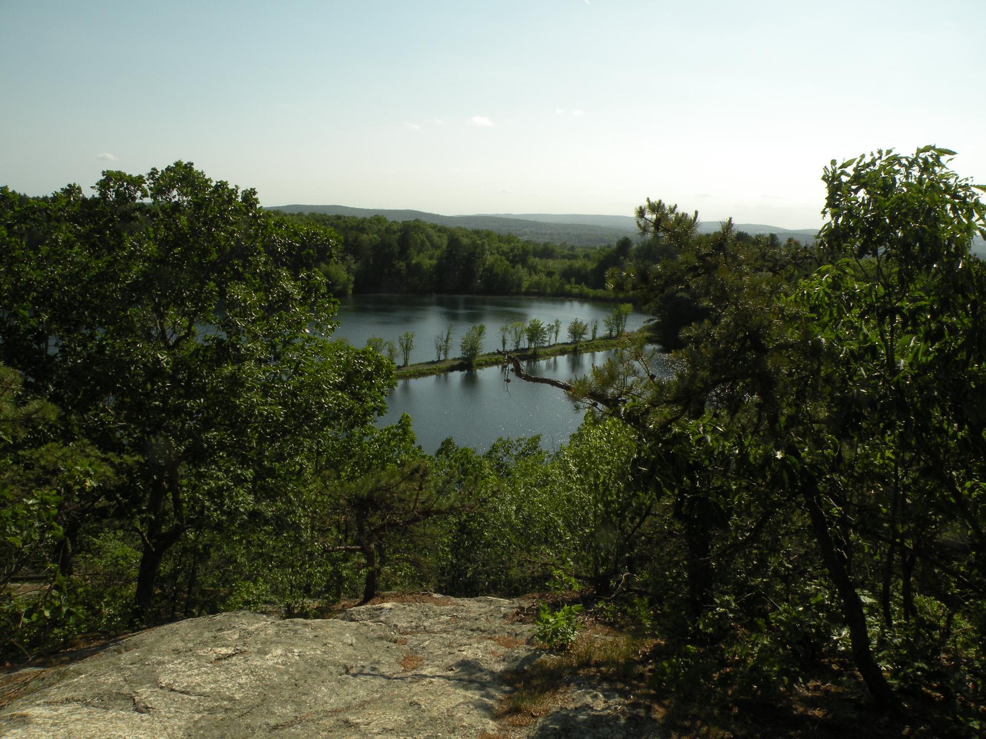 Overlook of a lake with a causeway, surrounded by green forest on a bright day.