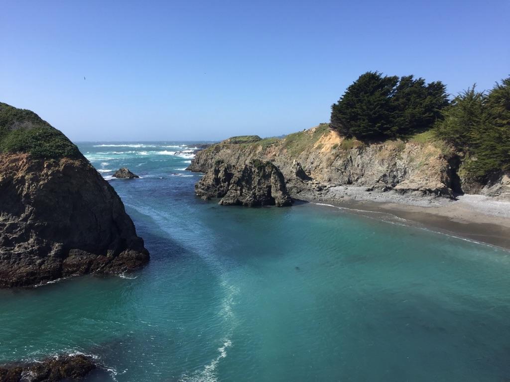 Bright blue cove with rocky shores and distant ocean under clear sky.