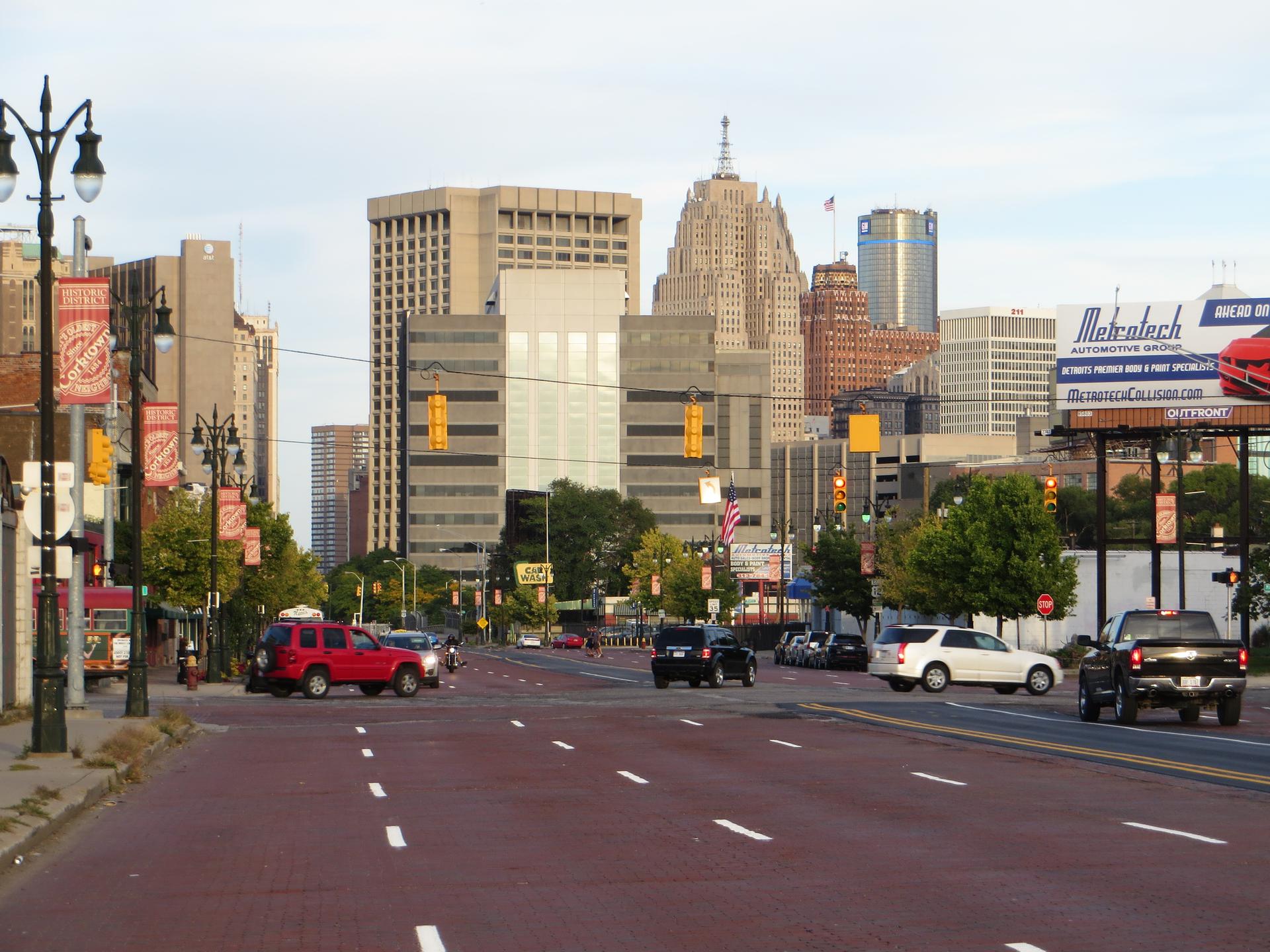 Busy city street with cars and tall buildings under a bright sky.