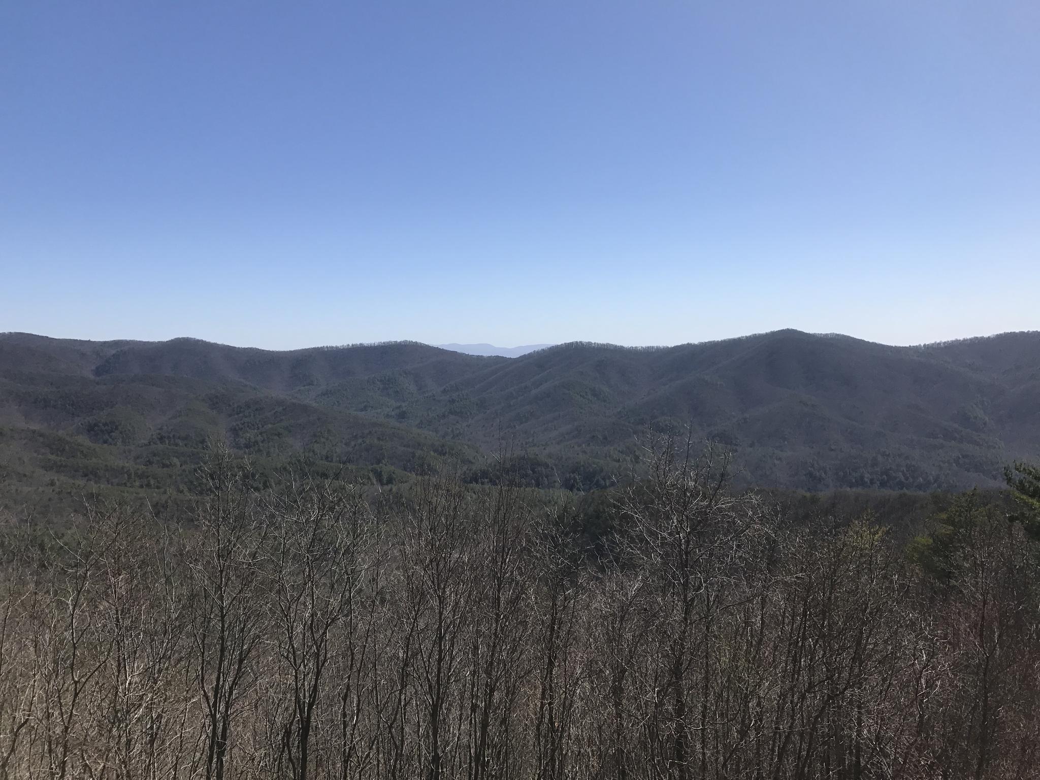 Expansive view of distant, forested mountains under a clear blue sky.