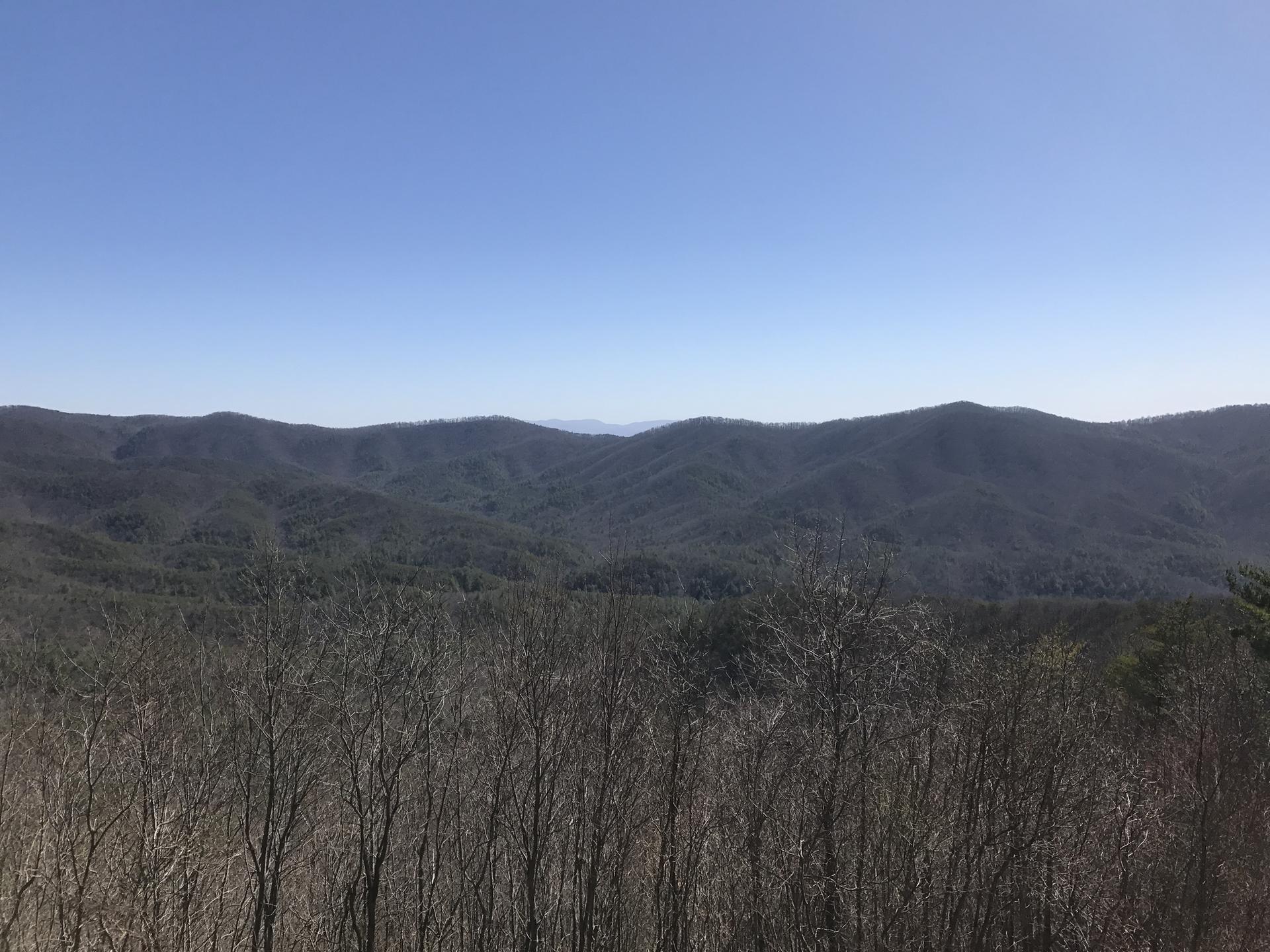 Expansive view of distant, forested mountains under a clear blue sky.