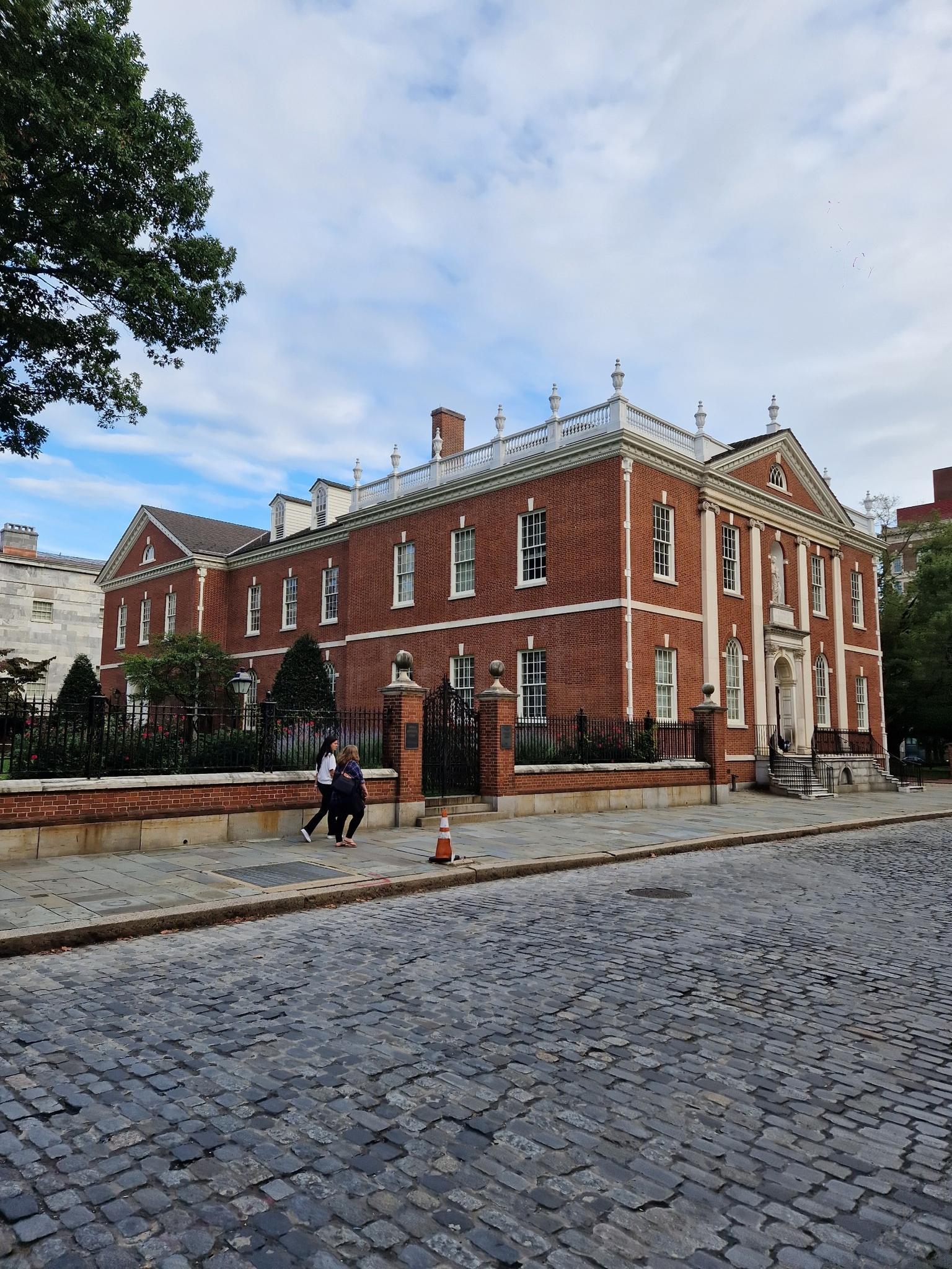 Historic brick building with white trim, cobblestone street, and two people walking.