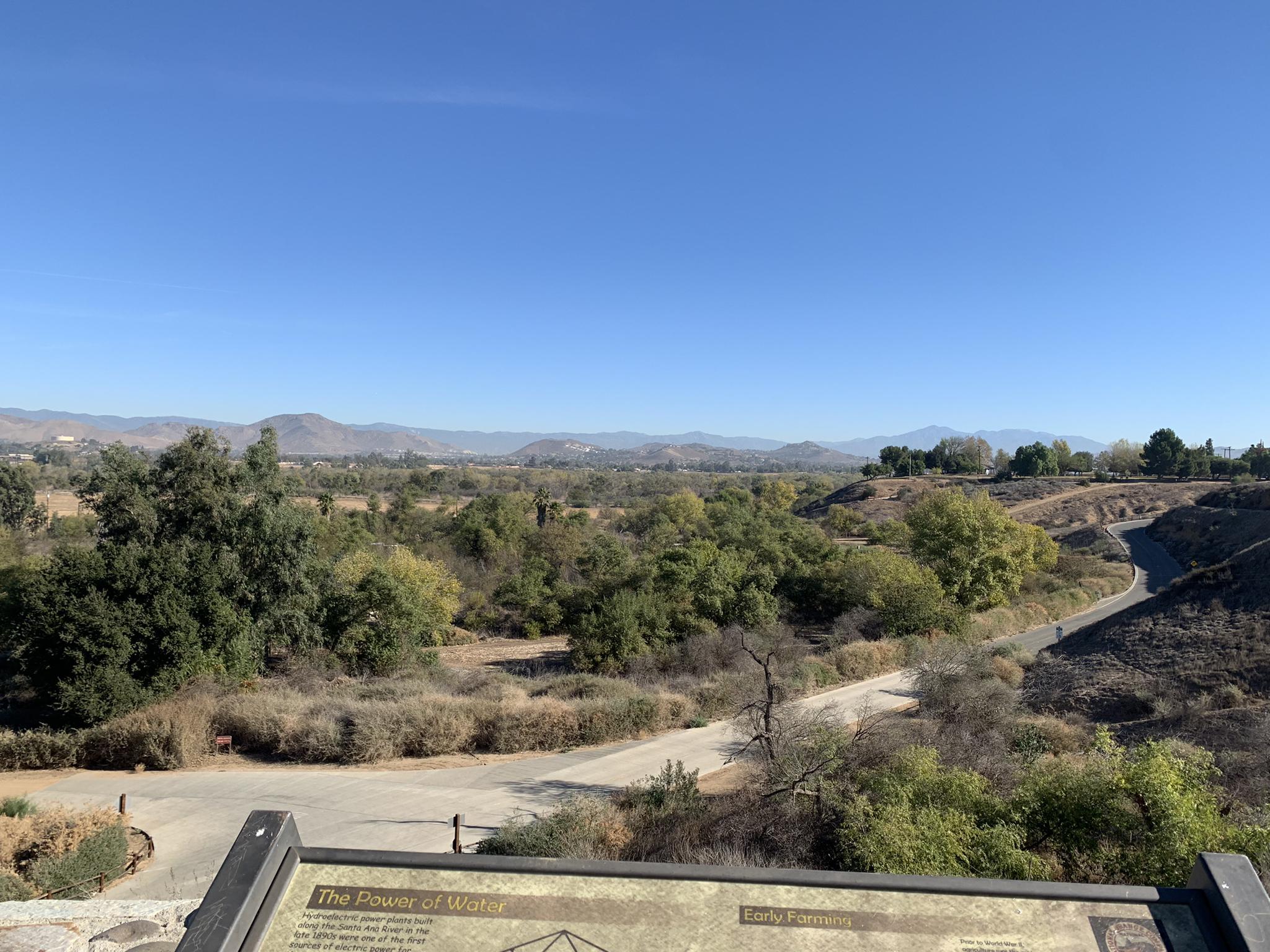 Panoramic view of a green valley, winding roads, distant mountains under a clear sky.