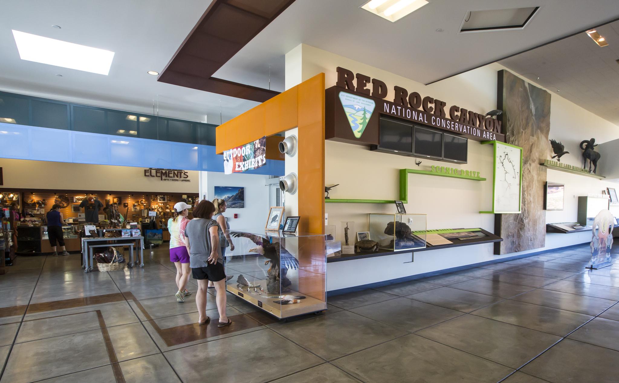 Indoor visitor center with people, exhibits, and a large sign.