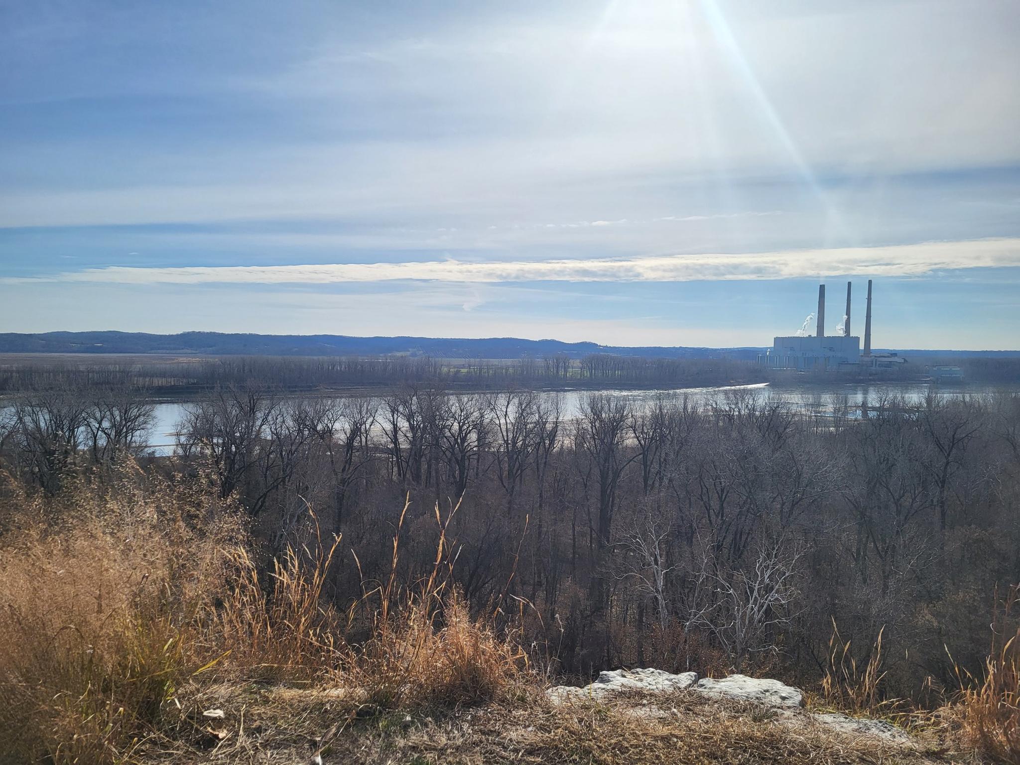 Sunny view of a river, industrial plant, and dry winter vegetation.