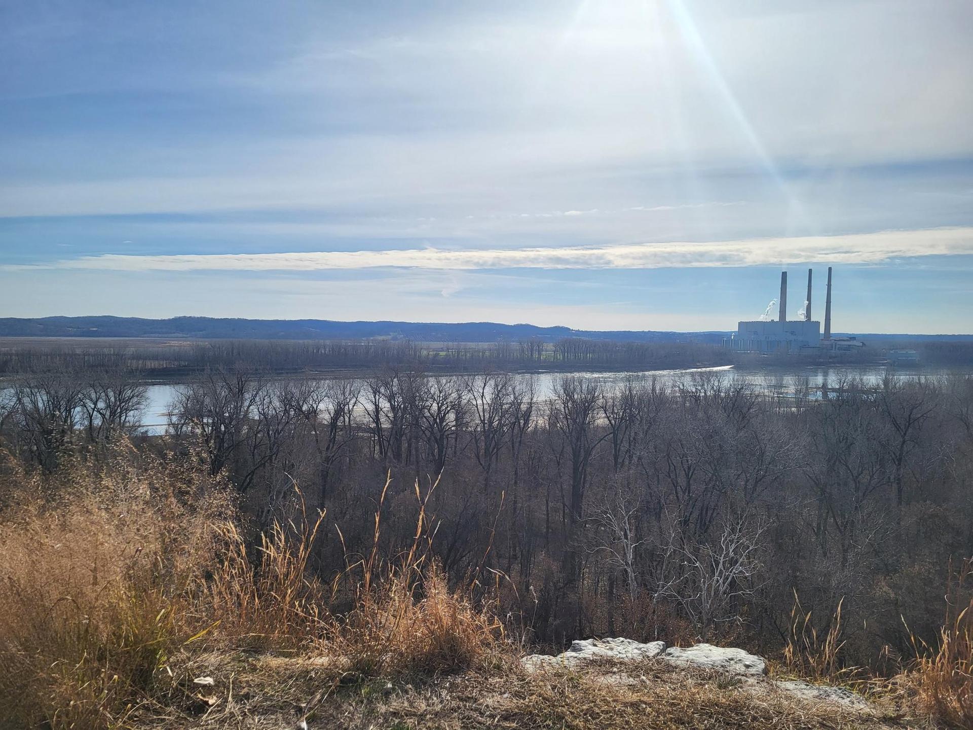 Sunny view of a river, industrial plant, and dry winter vegetation.
