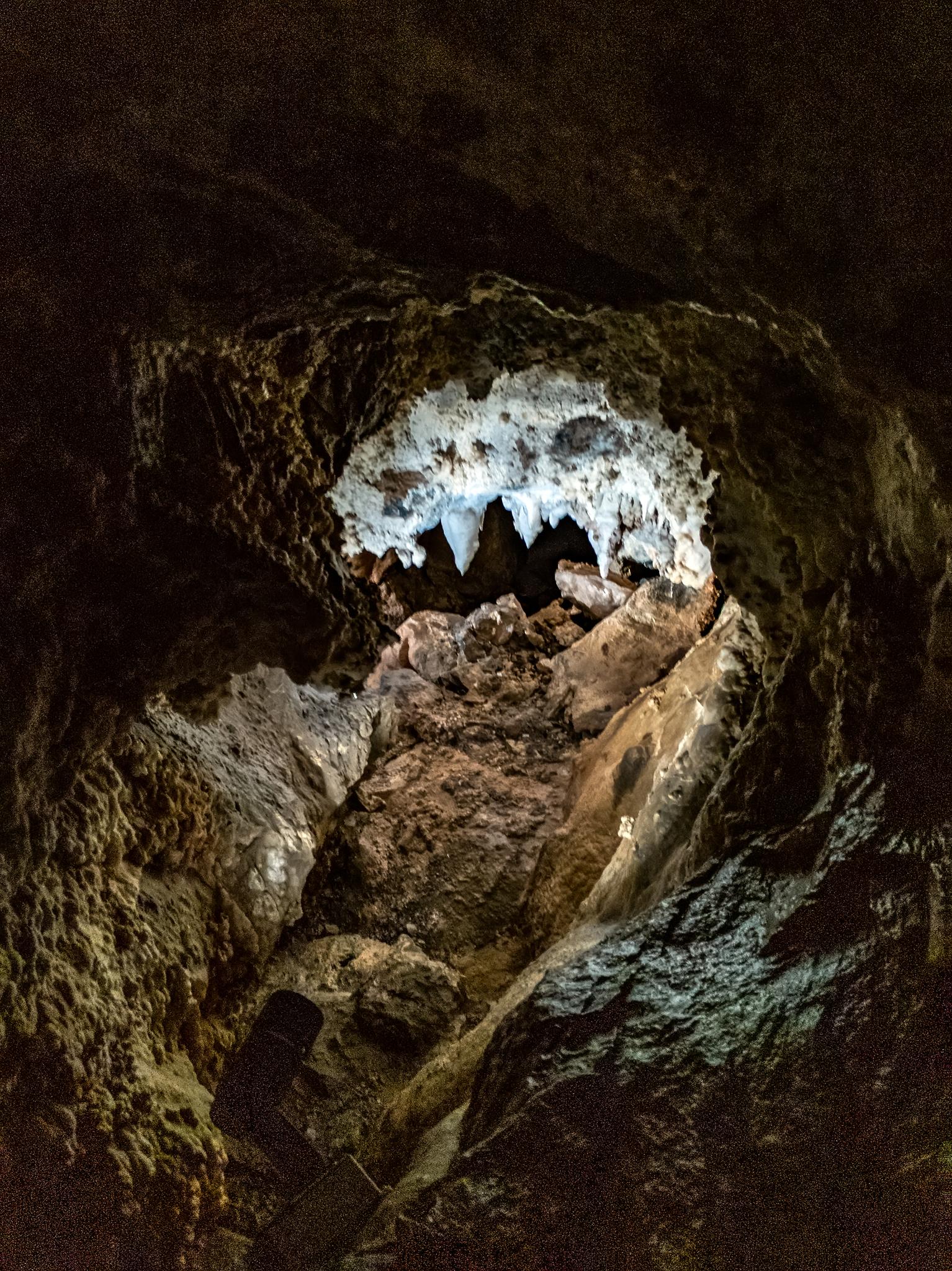 Dark cave interior with illuminated stalactites and rock formations.