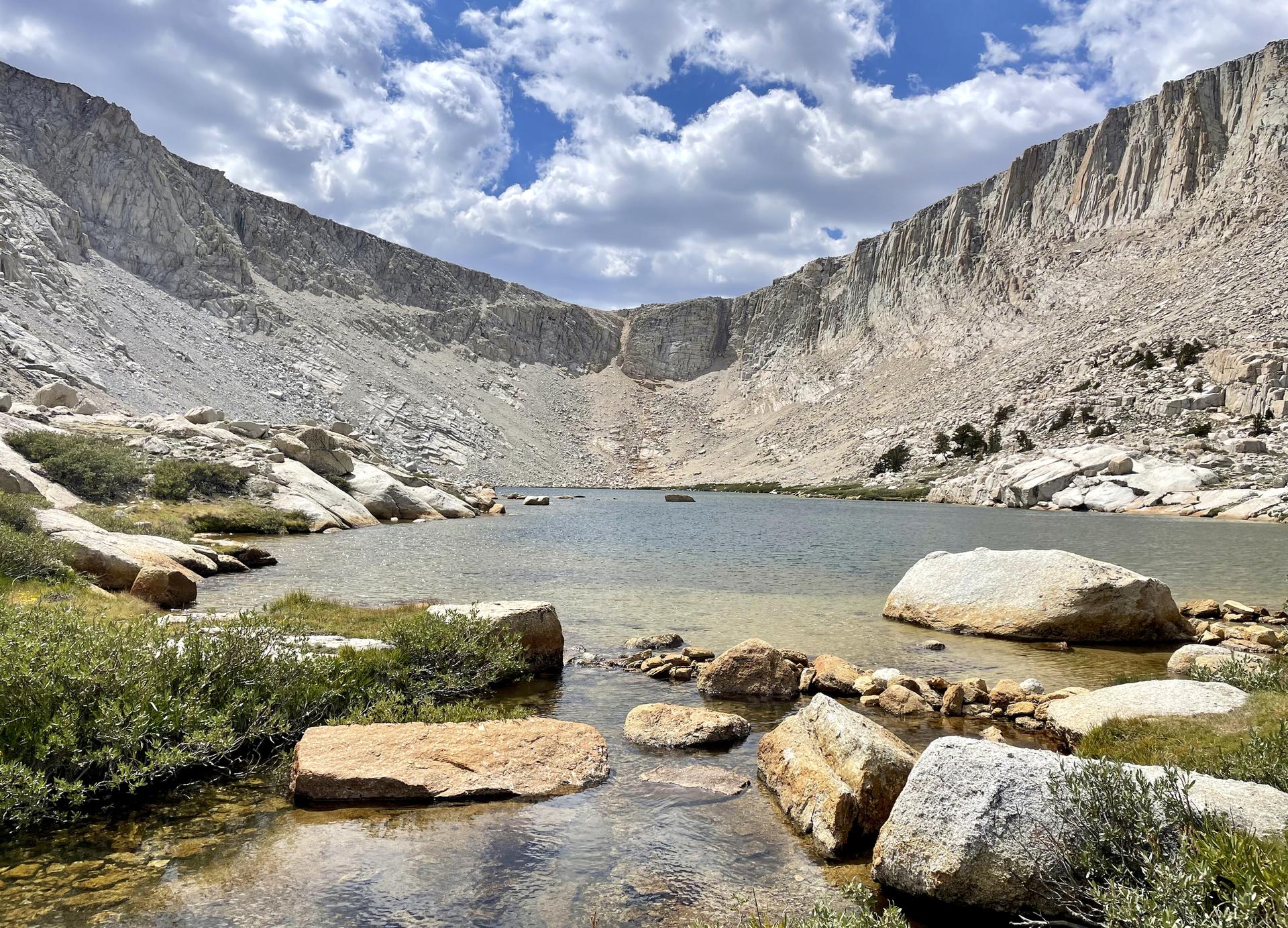 Calm lake surrounded by steep, rocky mountain walls under a partly cloudy sky.