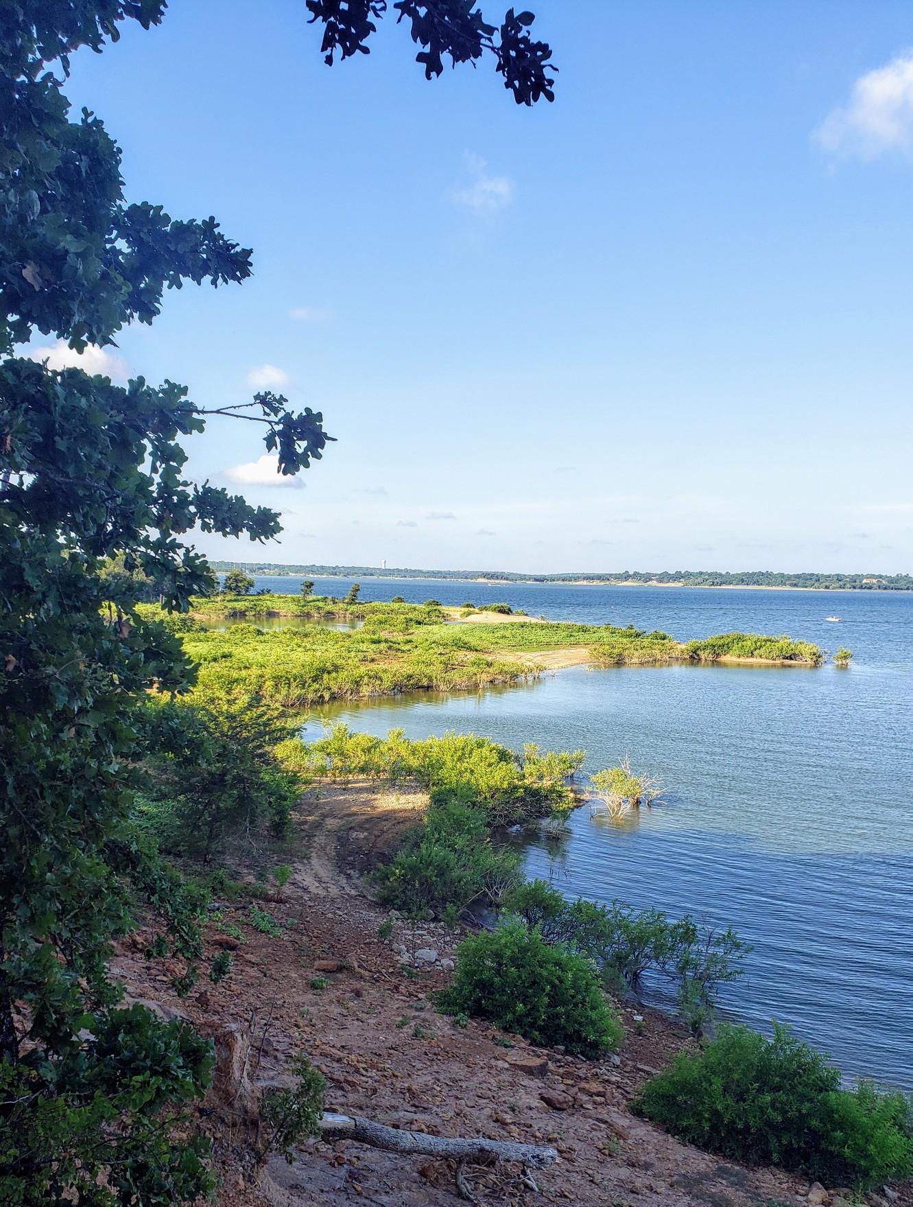 Bright sunny day over a large blue lake with green, tree-lined shores.