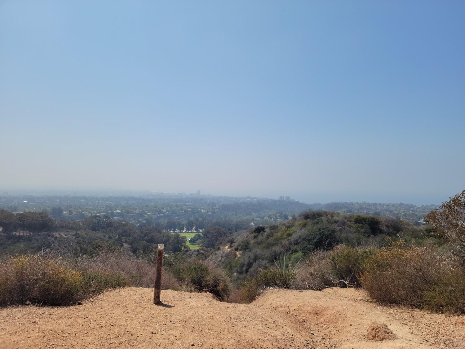 Sunny overlook of a distant city and green hills from a dirt path.