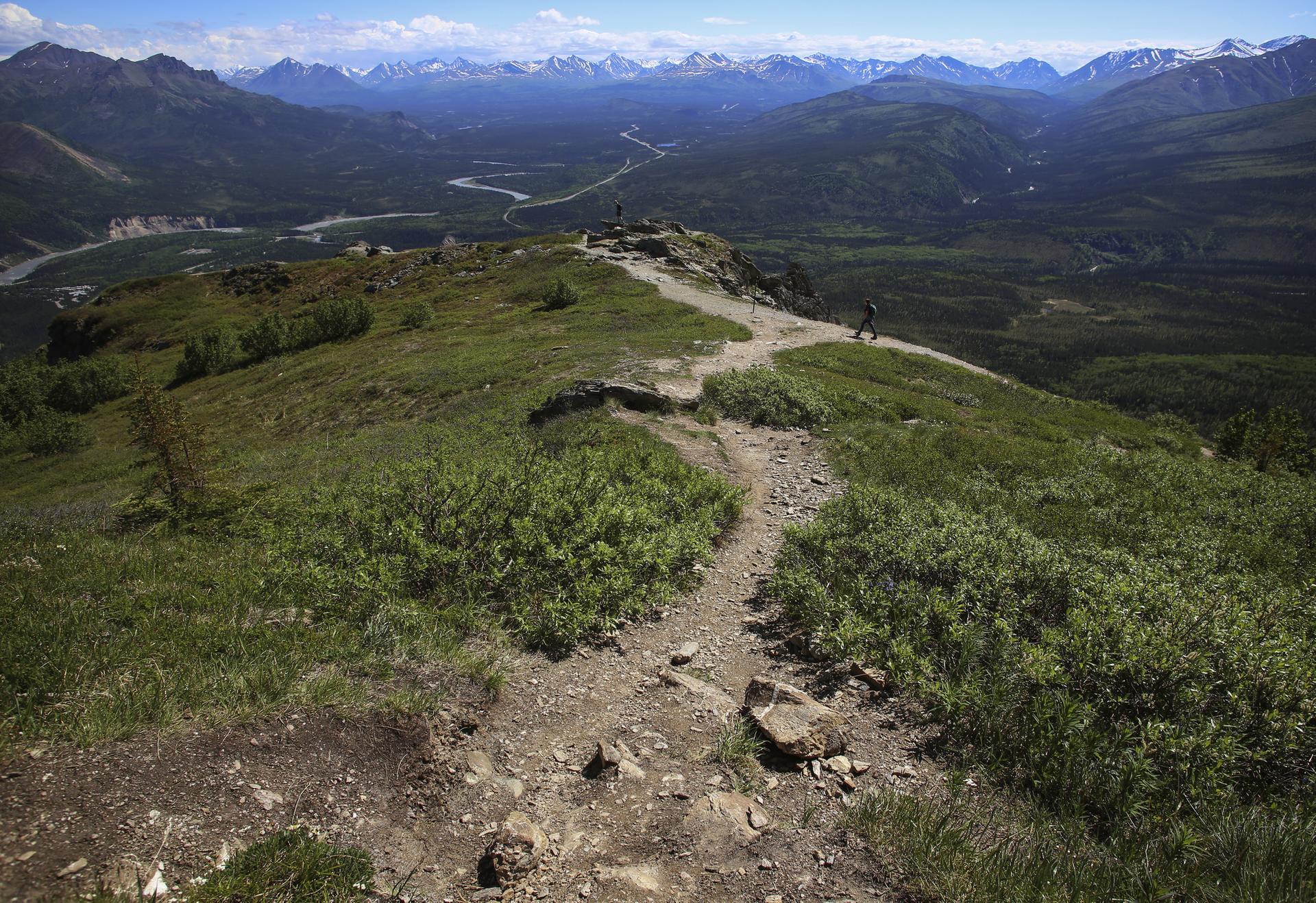 A winding dirt path on a grassy mountain ridge overlooks a vast valley.