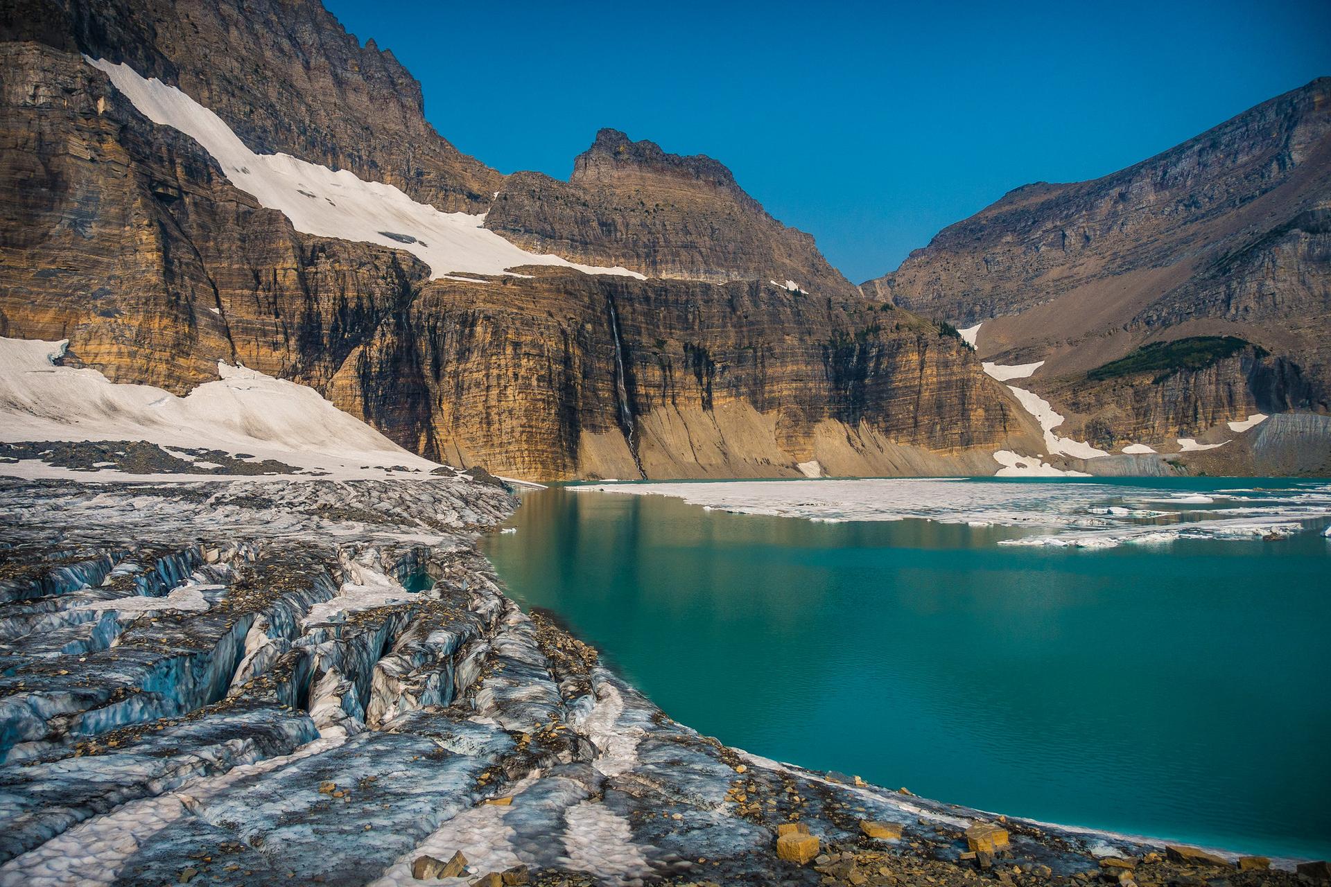 A vibrant turquoise lake with glacier ice, surrounded by rugged, snow-capped mountains.