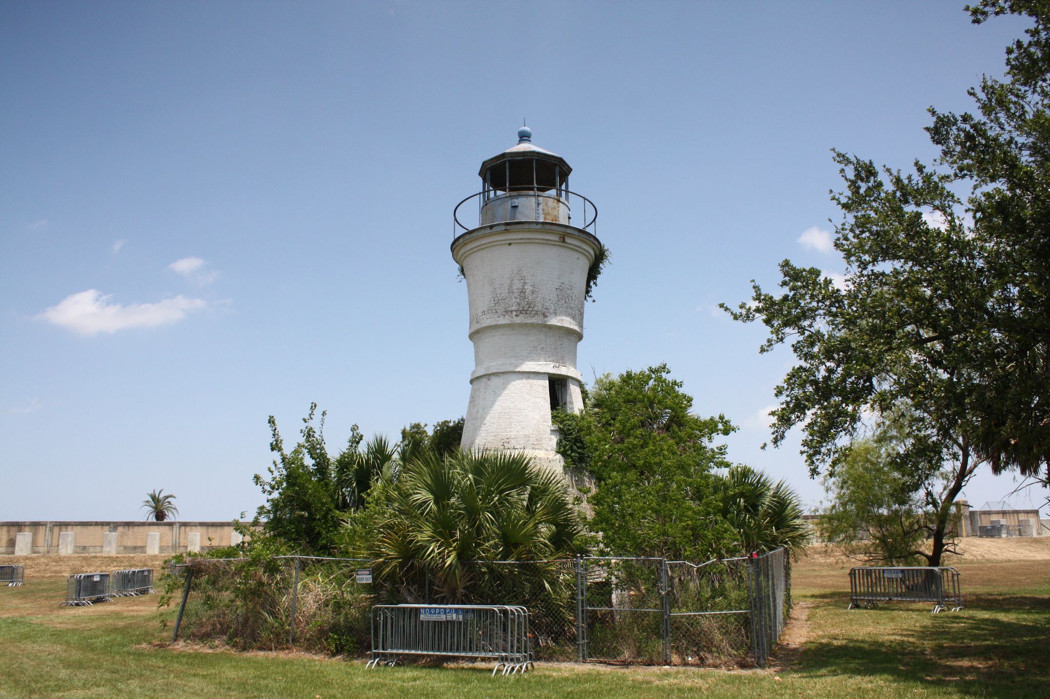 An old white lighthouse stands amidst green bushes under a clear blue sky. - Port Pontchartrain Lighthouse loop from University of New Orleans