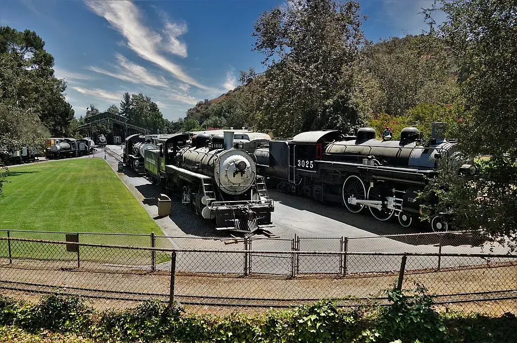 Two historic steam locomotives parked on tracks next to a grassy field.
