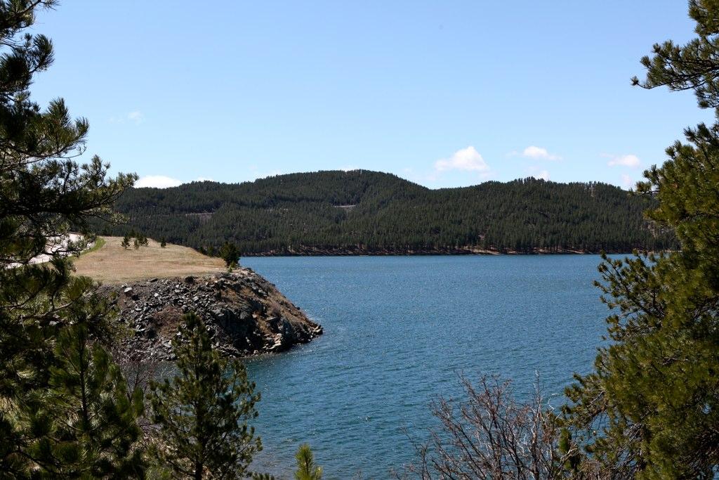 A clear blue lake surrounded by forested hills under a bright sky.