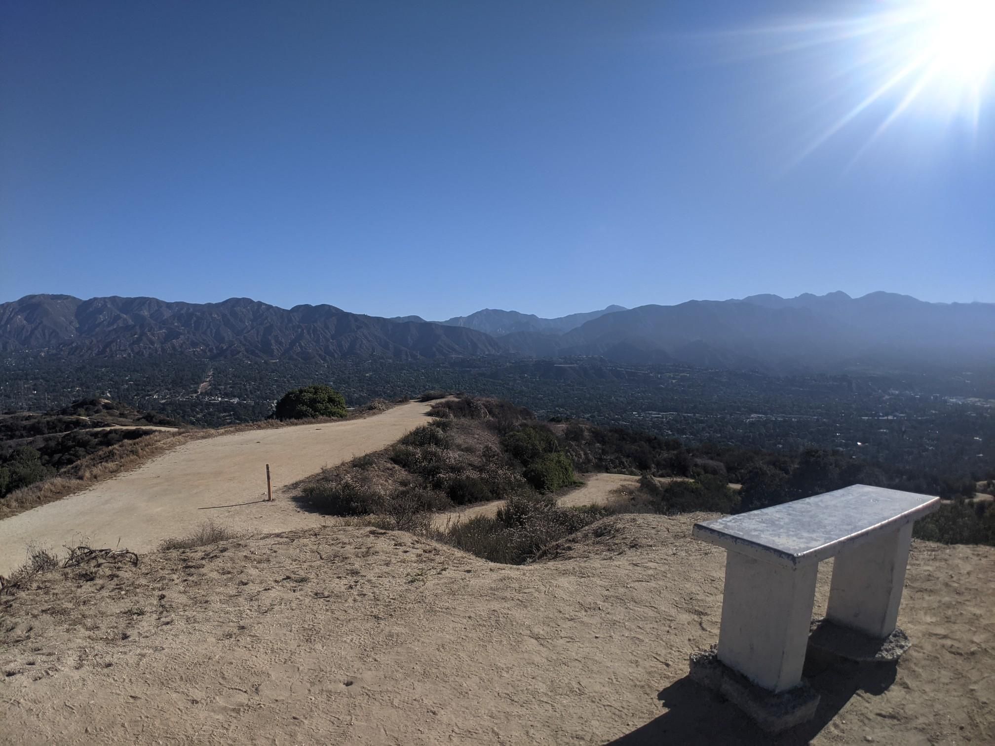 Sunny mountain view with a dirt path and a stone bench overlooking a valley. - Cherry Canyon Park and Lookout Tower