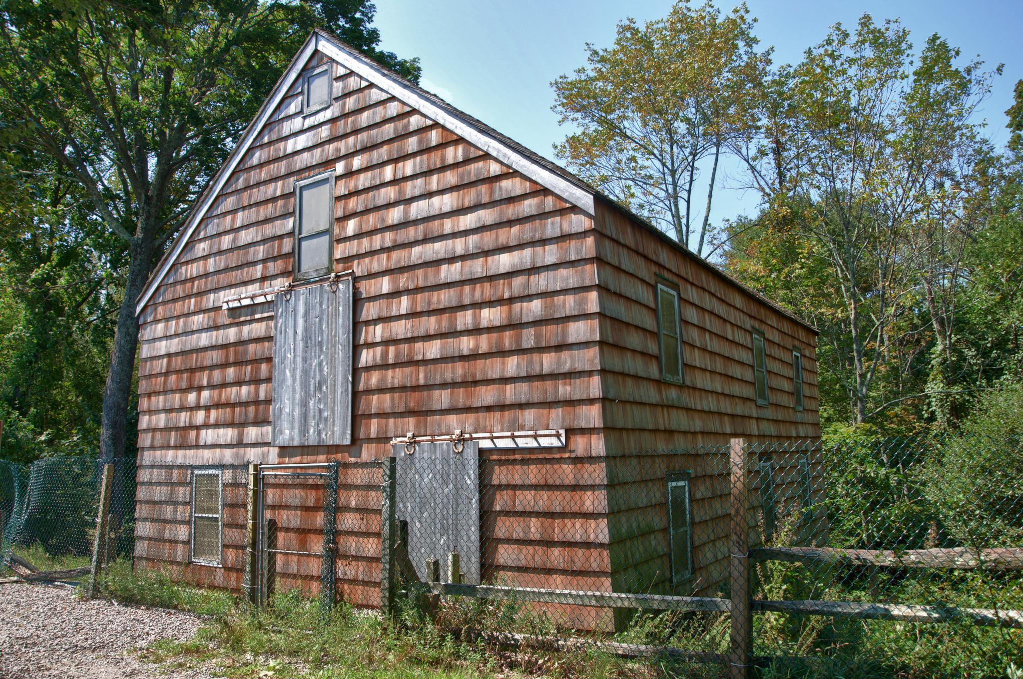 Rustic wooden barn with shingle siding, surrounded by trees, under bright daylight.