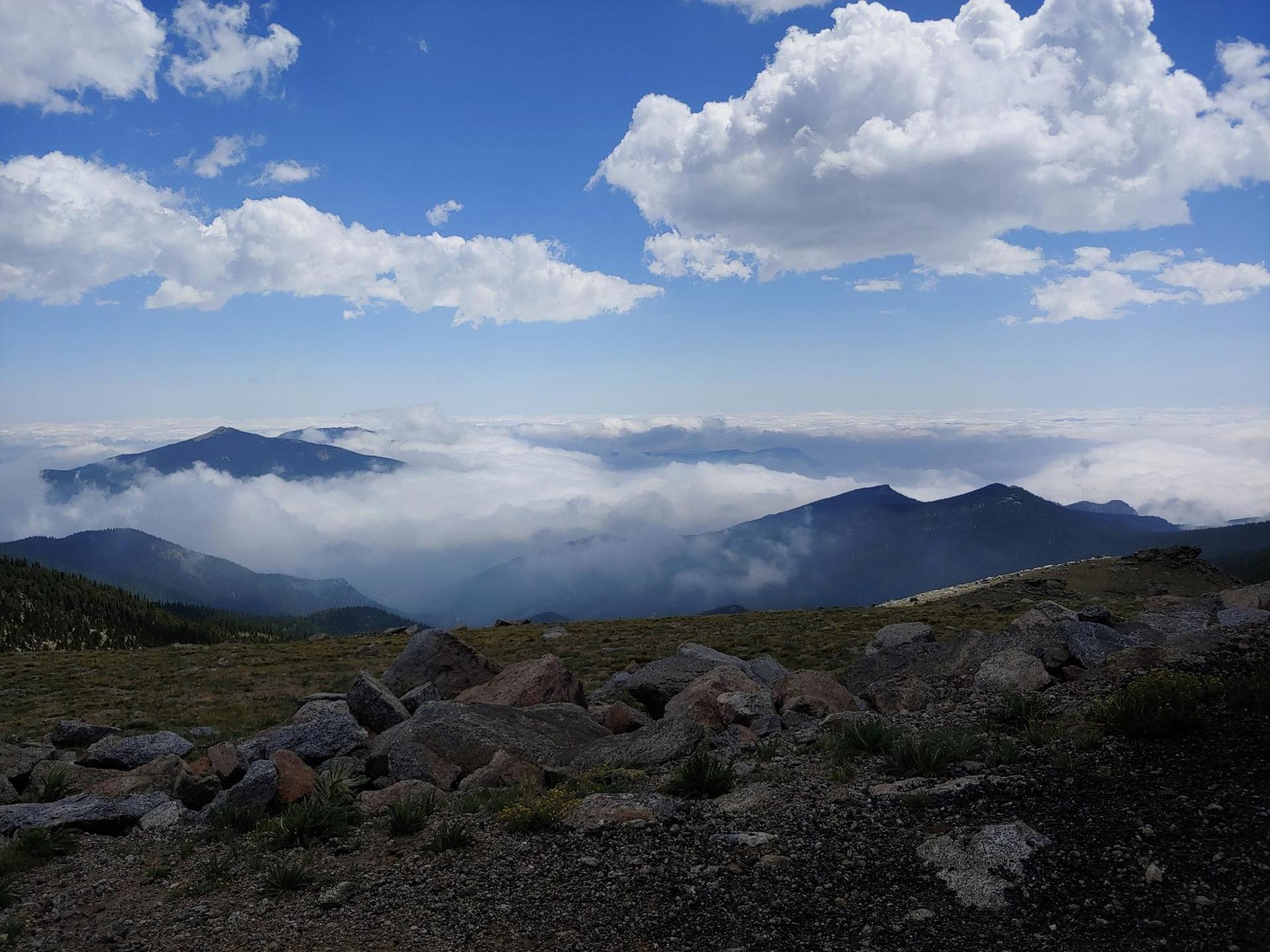 Mountain peaks rise above a vast cloud inversion under a bright sky.