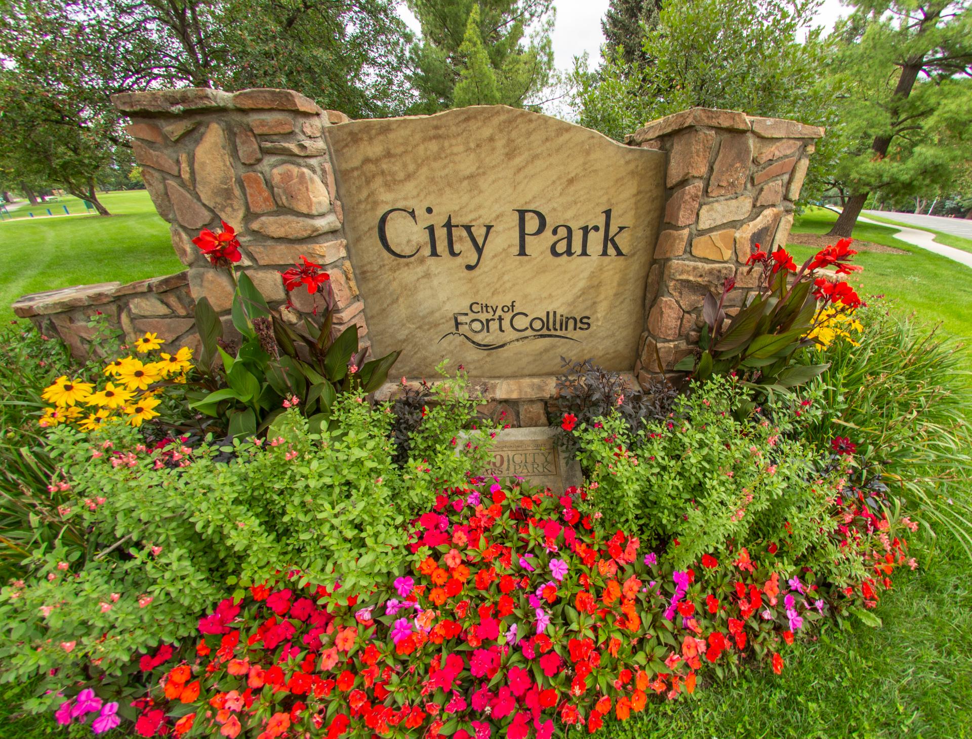 Stone sign surrounded by colorful flowers and green foliage under bright daylight.