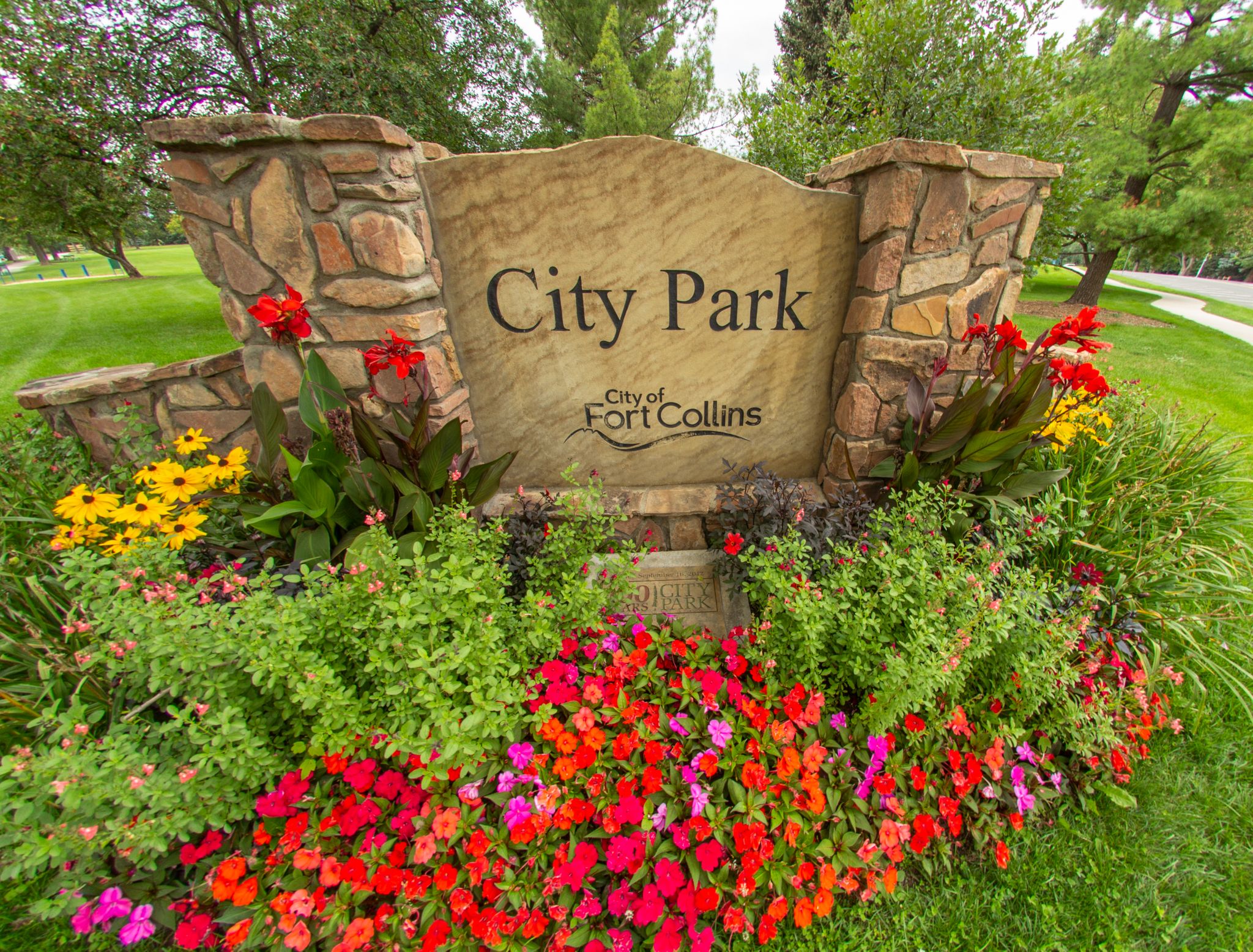 Stone sign surrounded by colorful flowers and green foliage under bright daylight. - Sheldon Lake (City Park Lake) loop from Fort Collins
