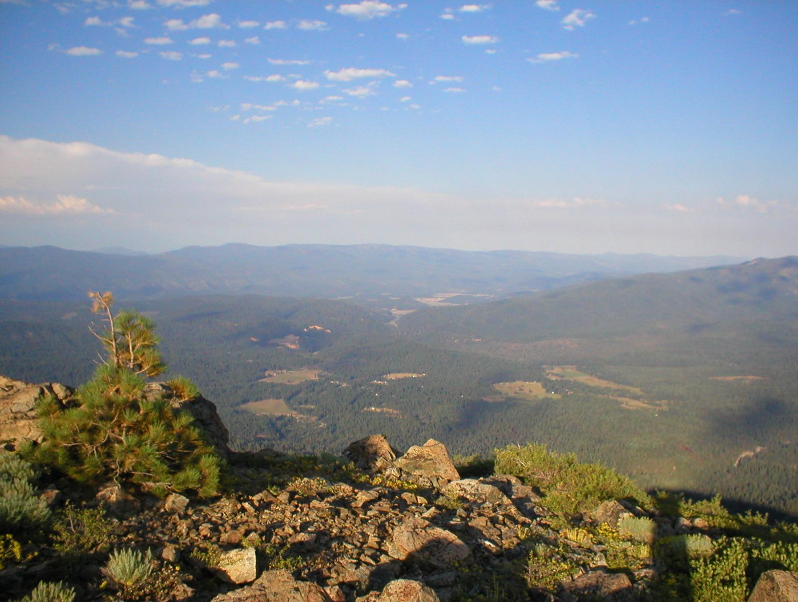 Expansive mountain landscape with a vast valley and distant hills under a blue sky.