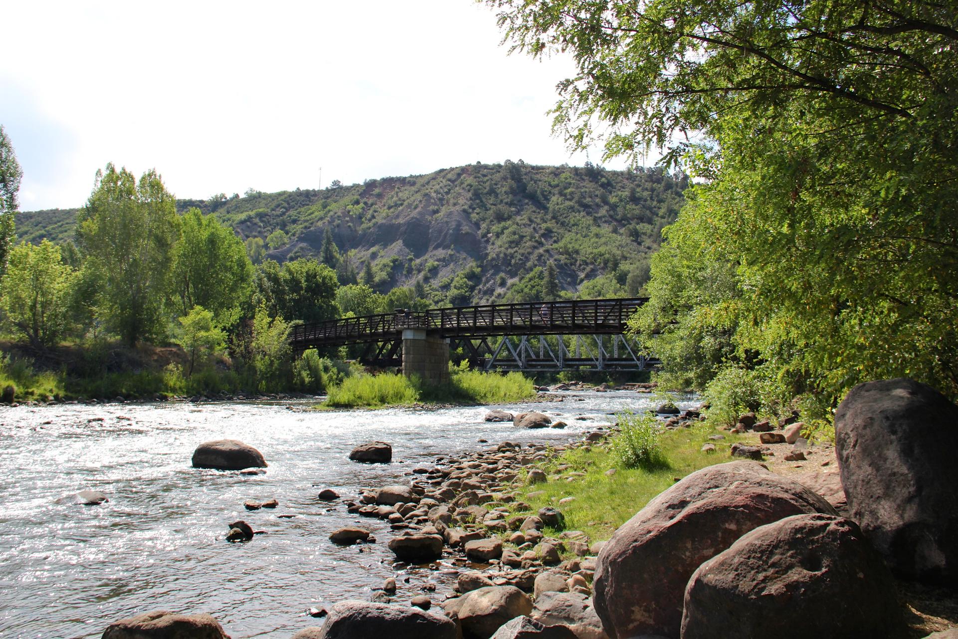 A river with rocks and a bridge, surrounded by green trees and hills.