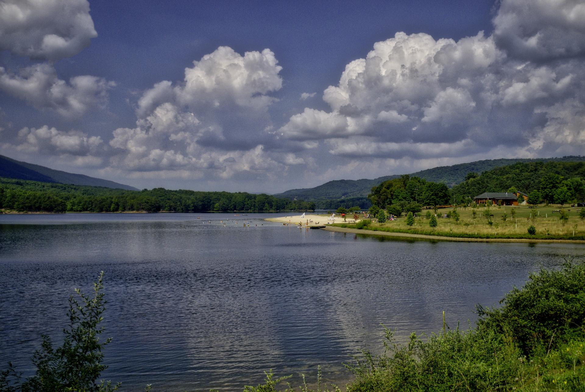 Sunny lake with distant hills, a sandy beach, and a building.