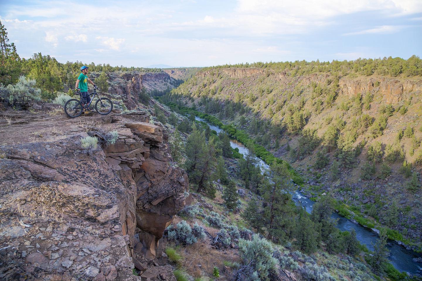 Mountain biker on a rocky cliff overlooking a deep river canyon with a winding river.