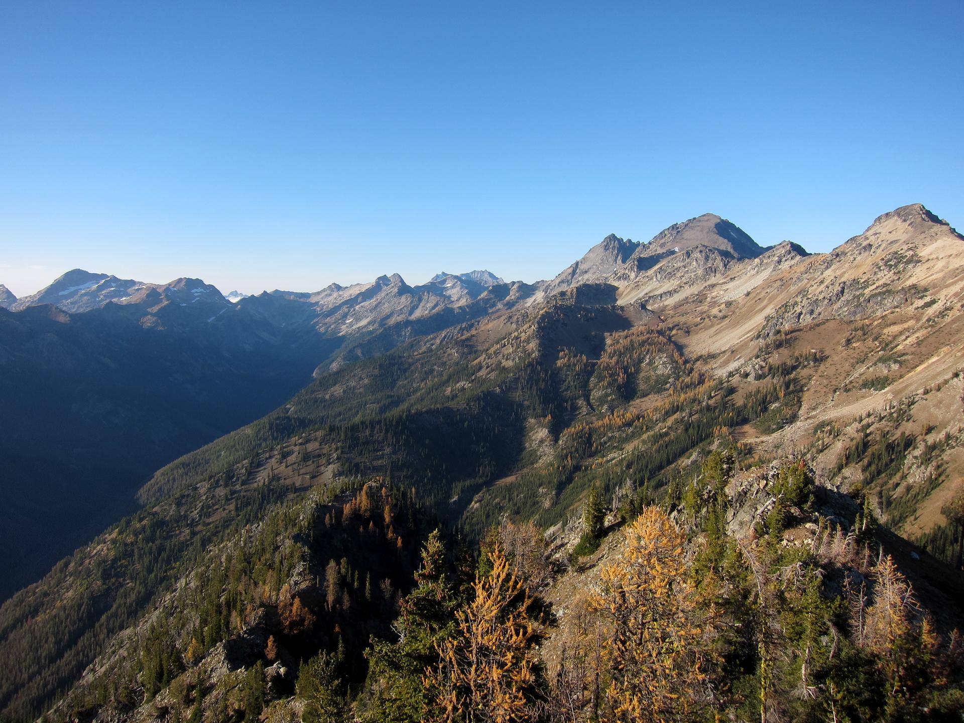 Sunny mountain vista showing a deep valley and forested slopes with autumn foliage.