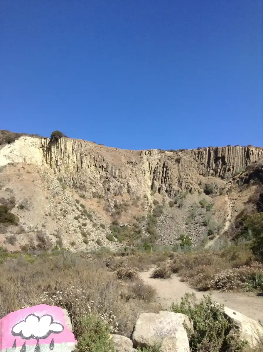A large, eroded cliff face overlooks dry scrubland, with a painted rock.