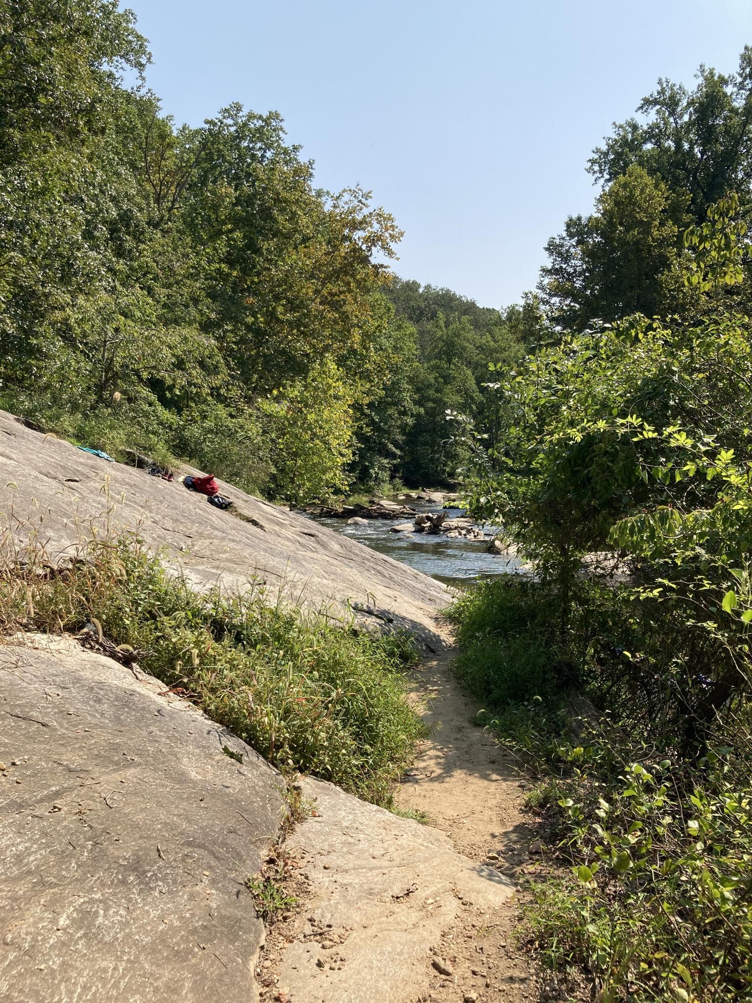 A dirt path alongside a rocky riverbank under a clear sky. - McKeldin Falls – McKeldin Rapids Trail loop from Patapsco Valley State Park