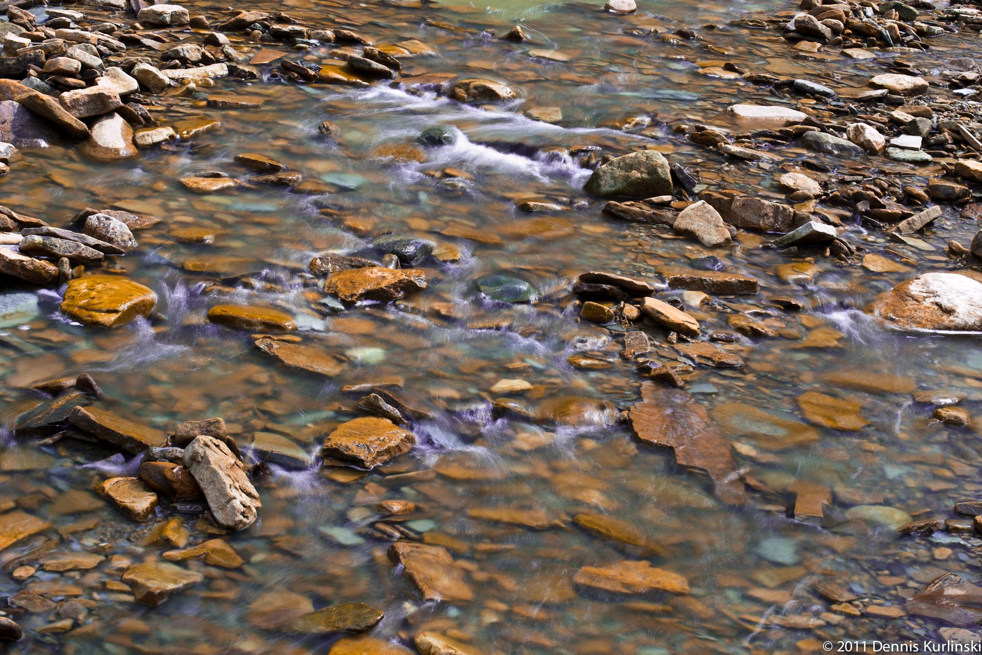 Clear water flows over colorful, flat rocks in a shallow stream.