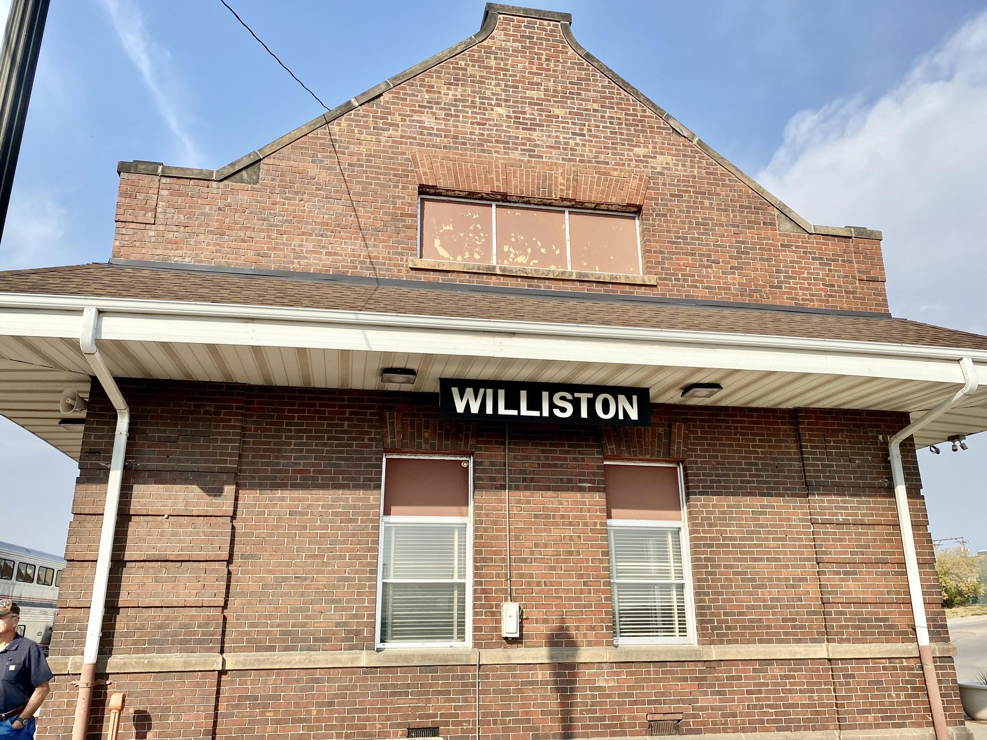 A brick building with a sign under a bright sky, person visible left.